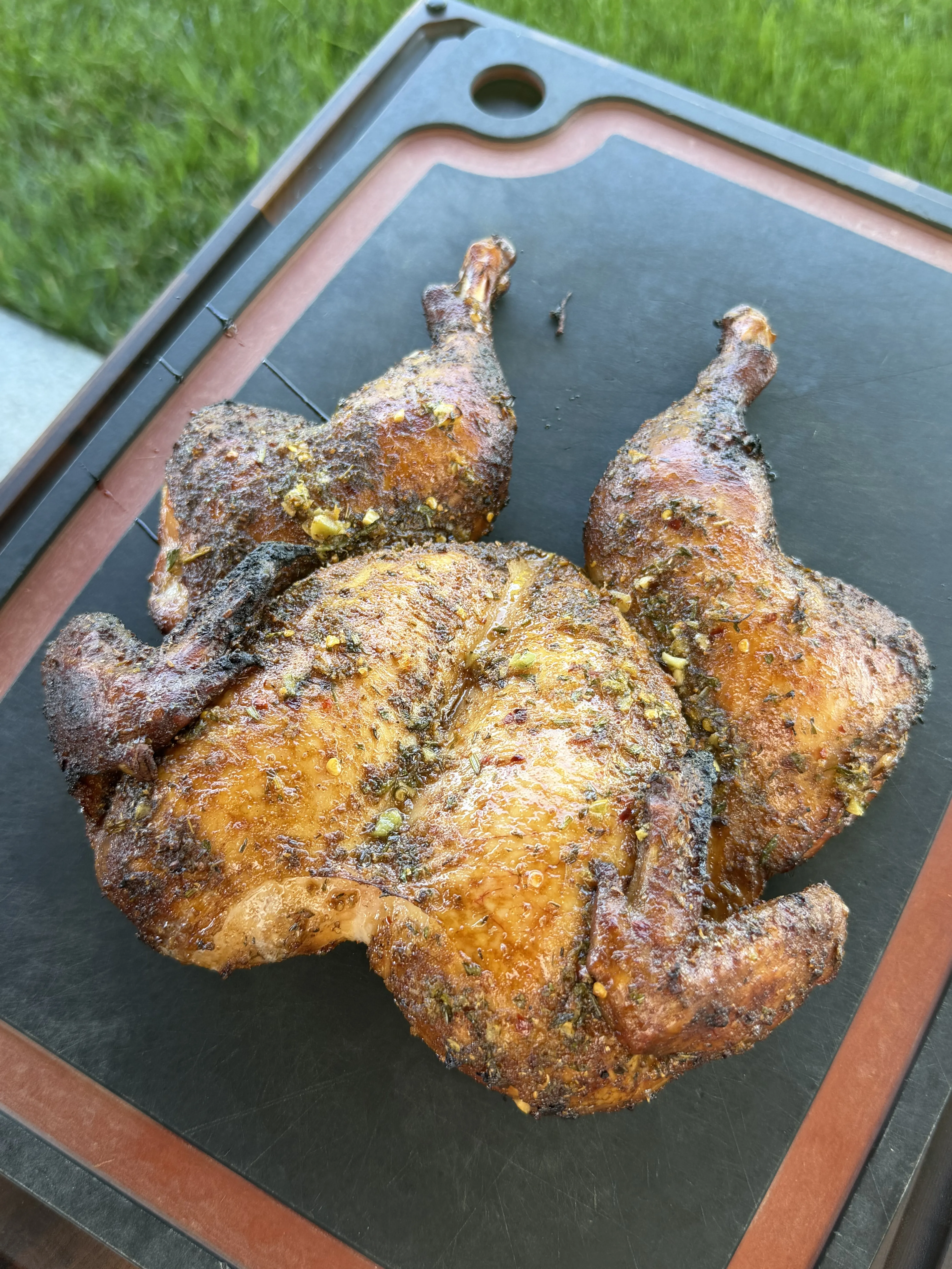 Two whole grilled lemon garlic herb spatchcock chickens with crispy skin resting on a cutting board