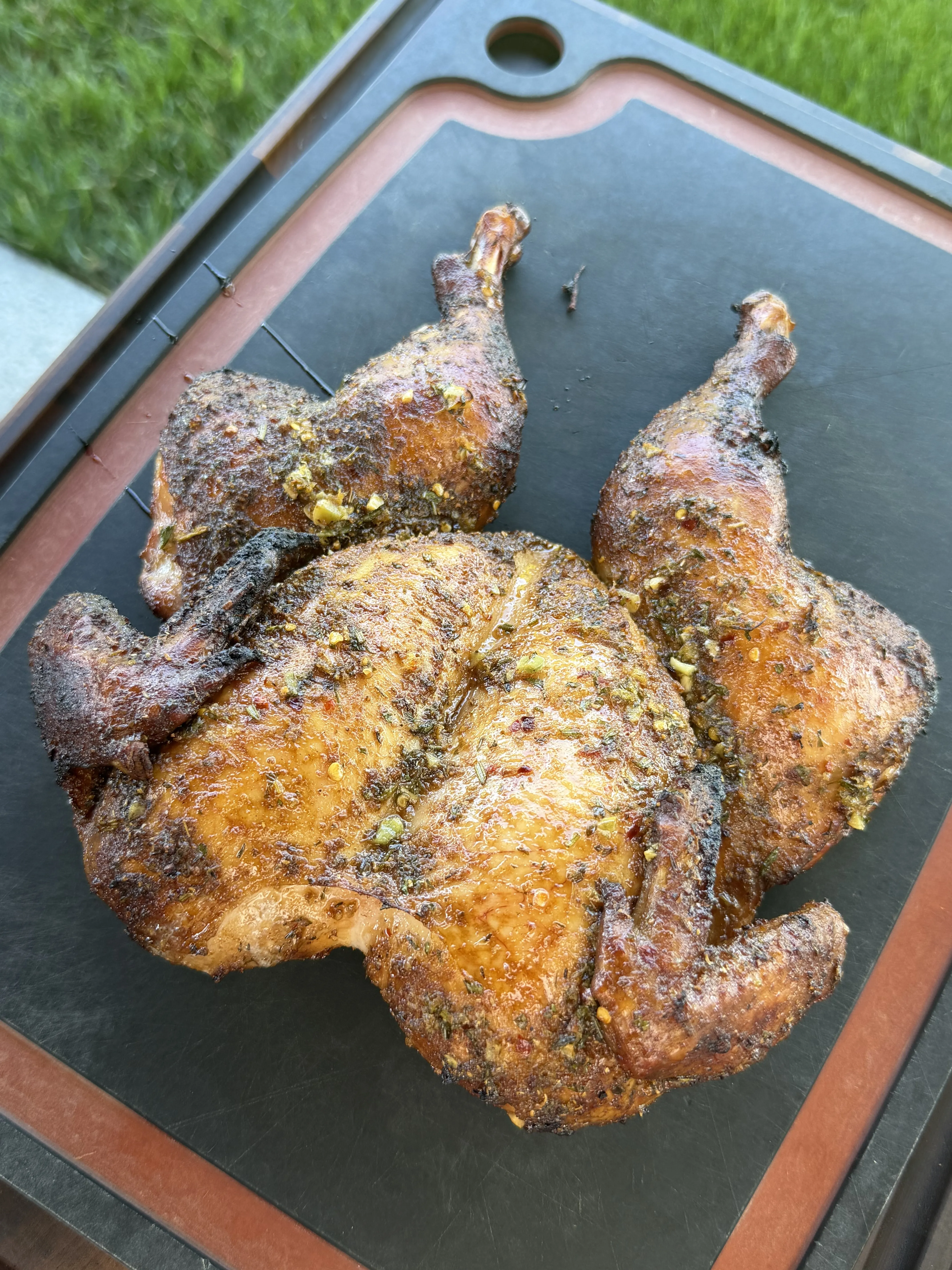 Whole spatchcock chicken with golden crispy skin grilling on outdoor charcoal grill grates