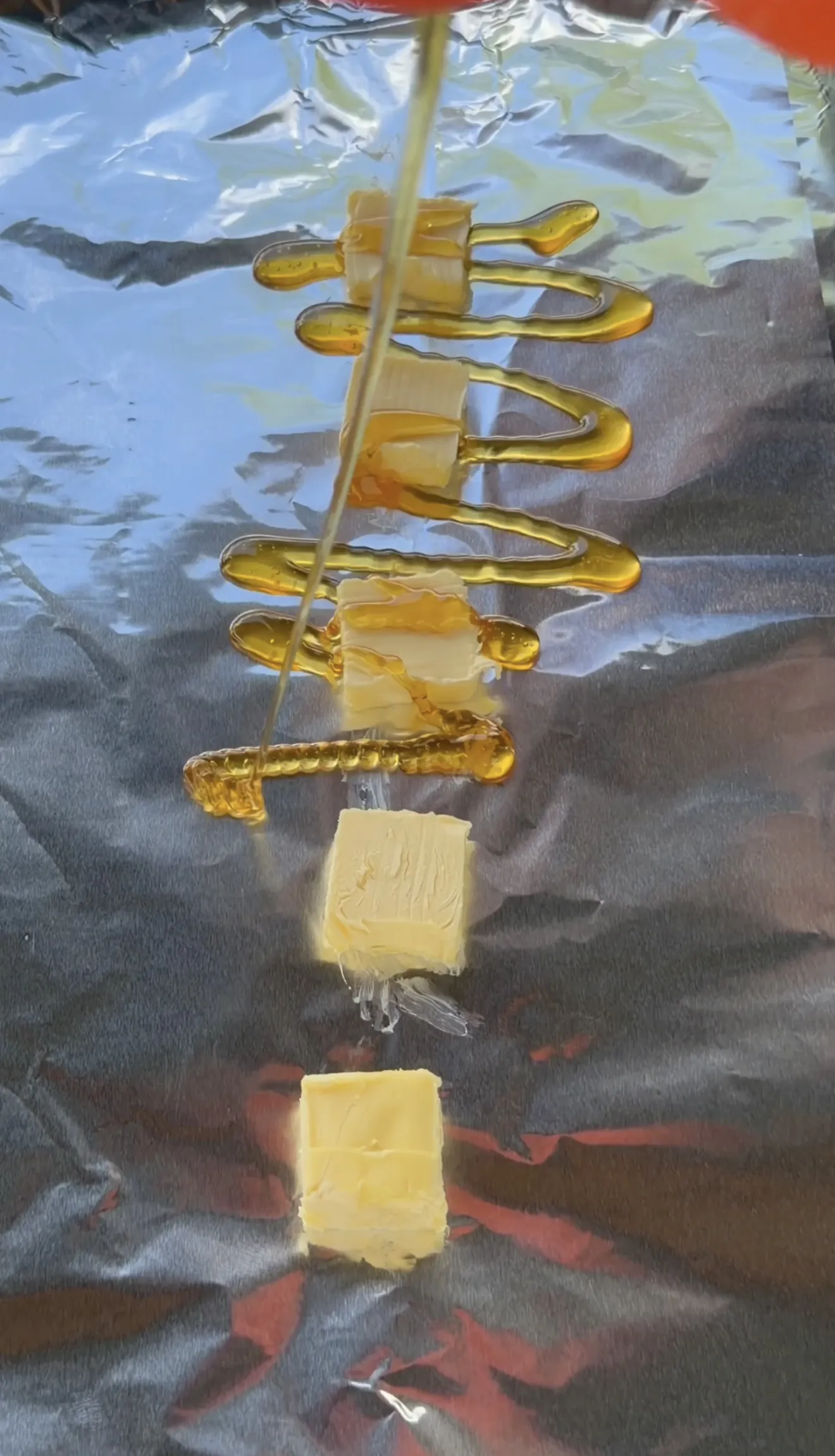 Honey being drizzled over butter pats on foil for the competition rib wrap