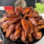 a pile of hot honey glazed lemon pepper chicken wings arranged on a cast iron skillet, an outdoor grill in the background.