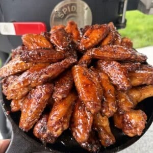 a pile of hot honey glazed lemon pepper chicken wings arranged on a cast iron skillet, an outdoor grill in the background.