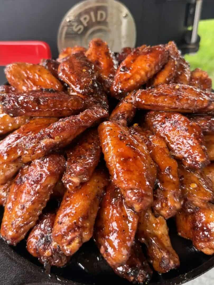 a pile of hot honey glazed lemon pepper chicken wings arranged on a cast iron skillet, an outdoor grill in the background.
