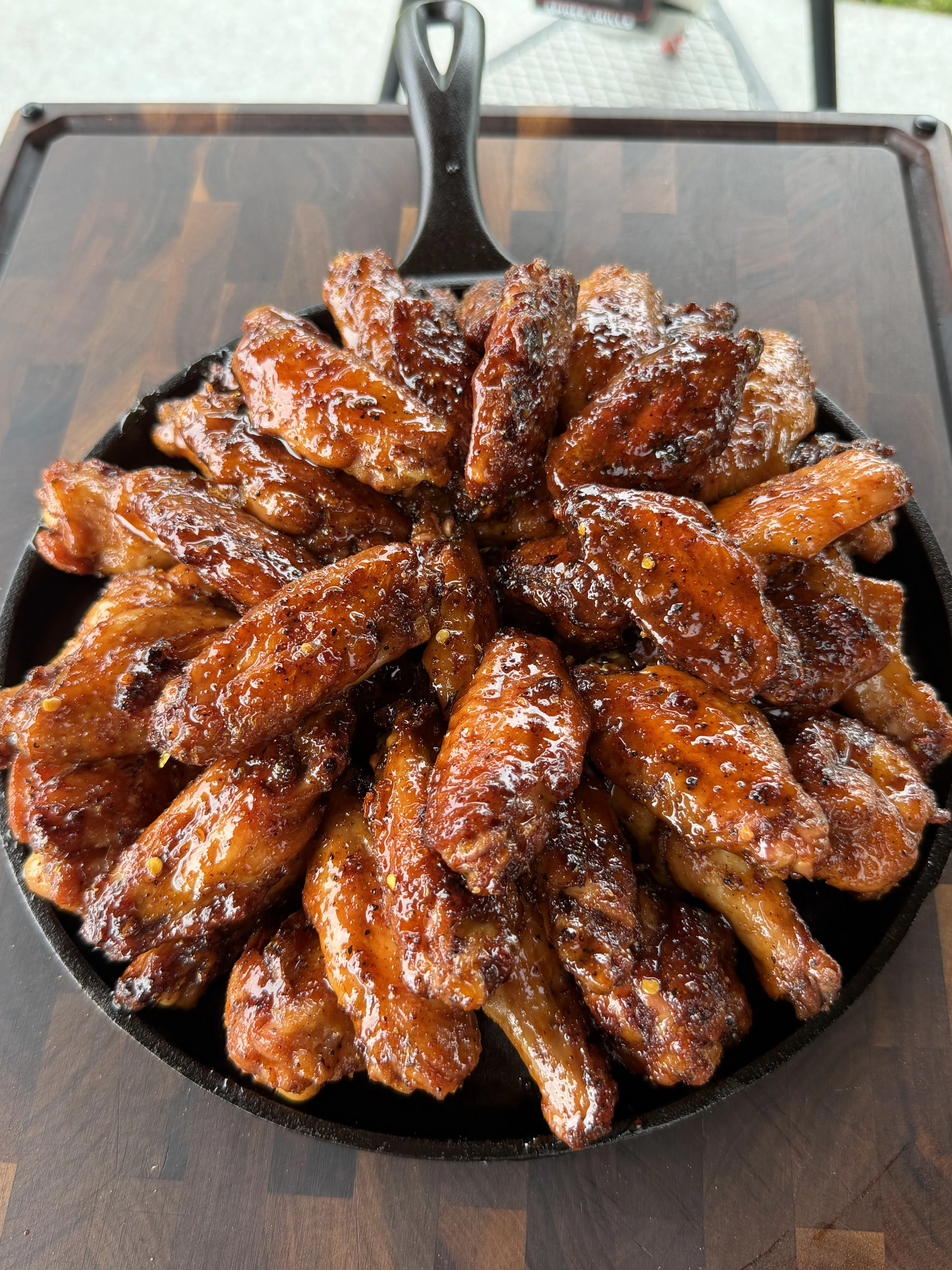 Glazed hot honey lemon pepper wings in a cast iron skillet on a wooden surface