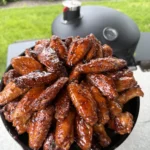 Glazed hot honey lemon pepper chicken wings arranged in a black cast iron skillet on outdoor grill