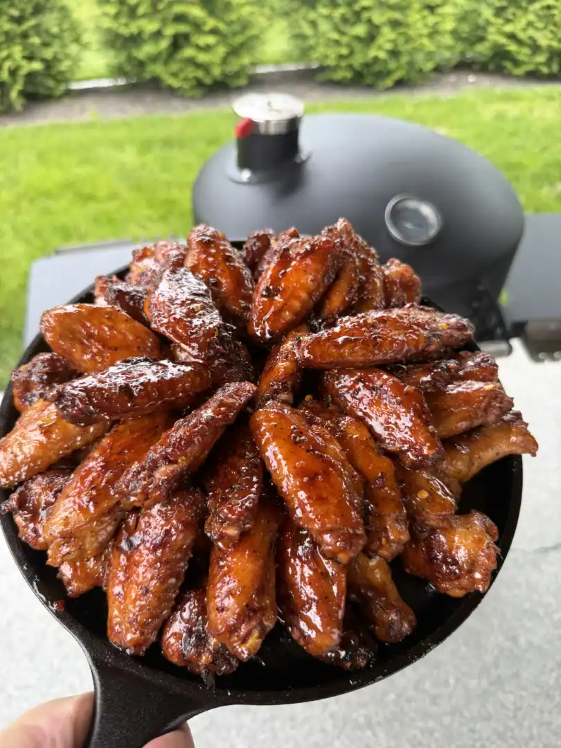Glazed hot honey lemon pepper chicken wings arranged in a black cast iron skillet on outdoor grill