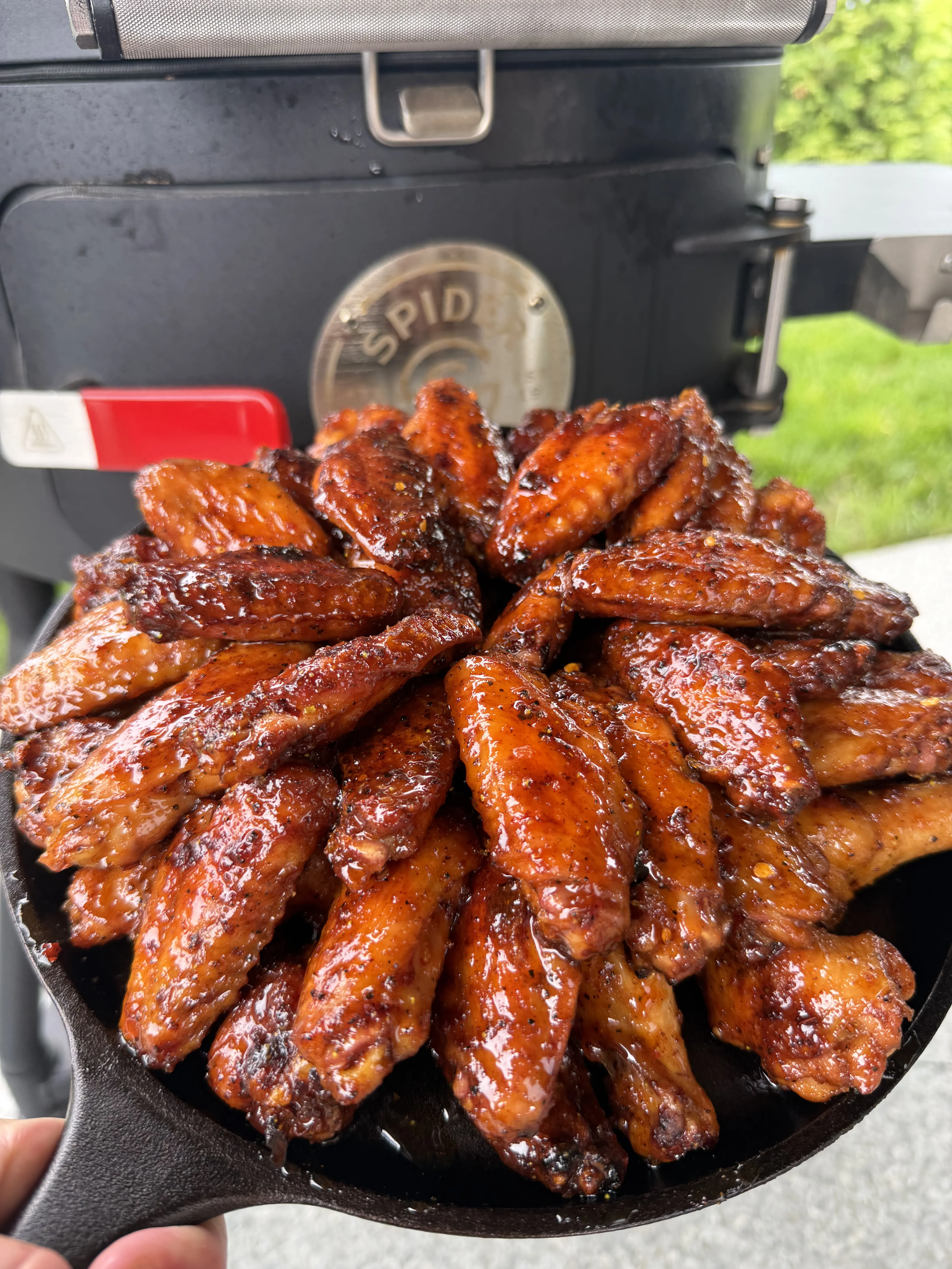 Finished glazed hot honey lemon pepper wings piled in a cast iron skillet on the grill