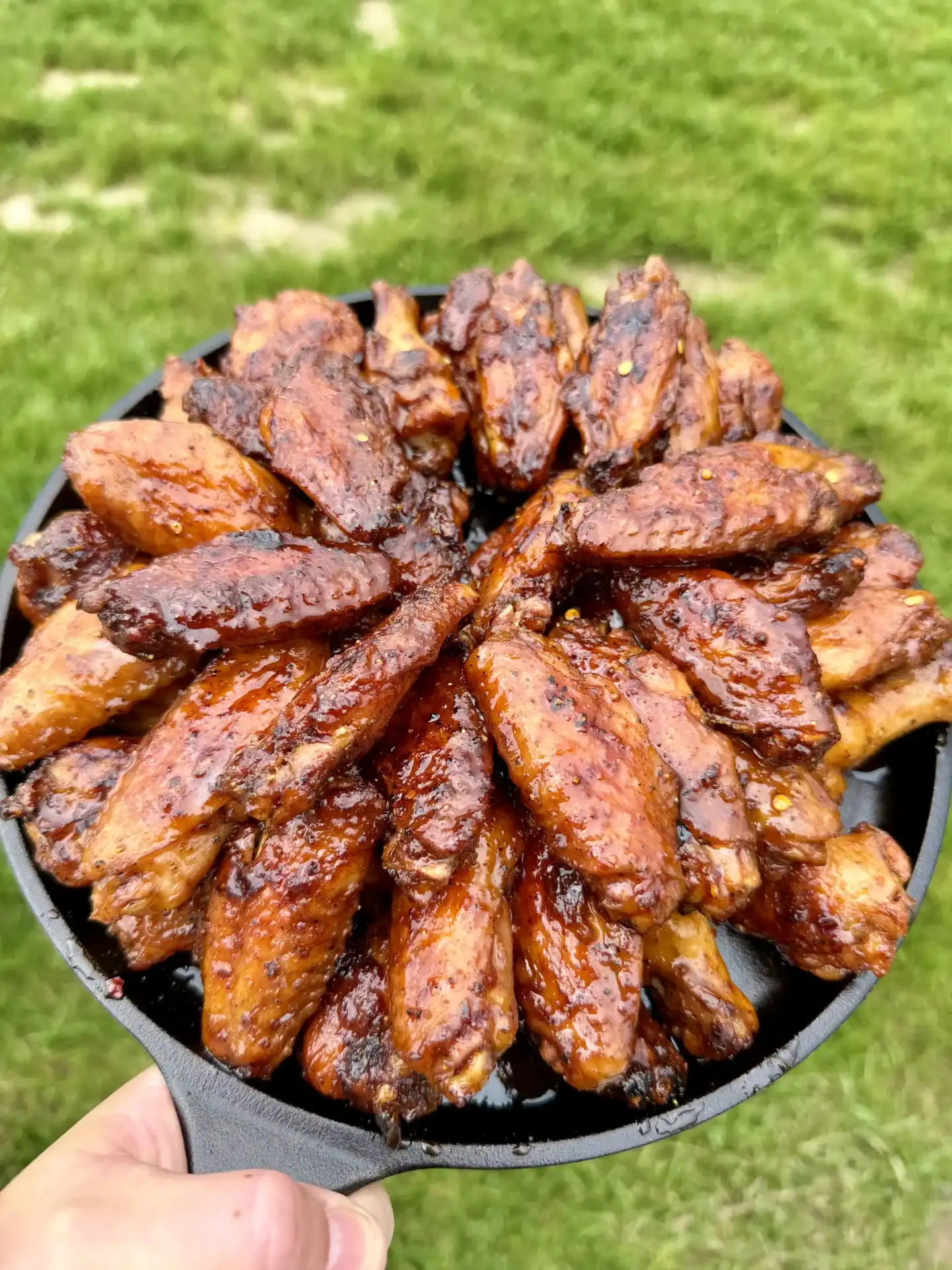 Golden brown hot honey chicken wings arranged in a black cast iron skillet held outdoors.