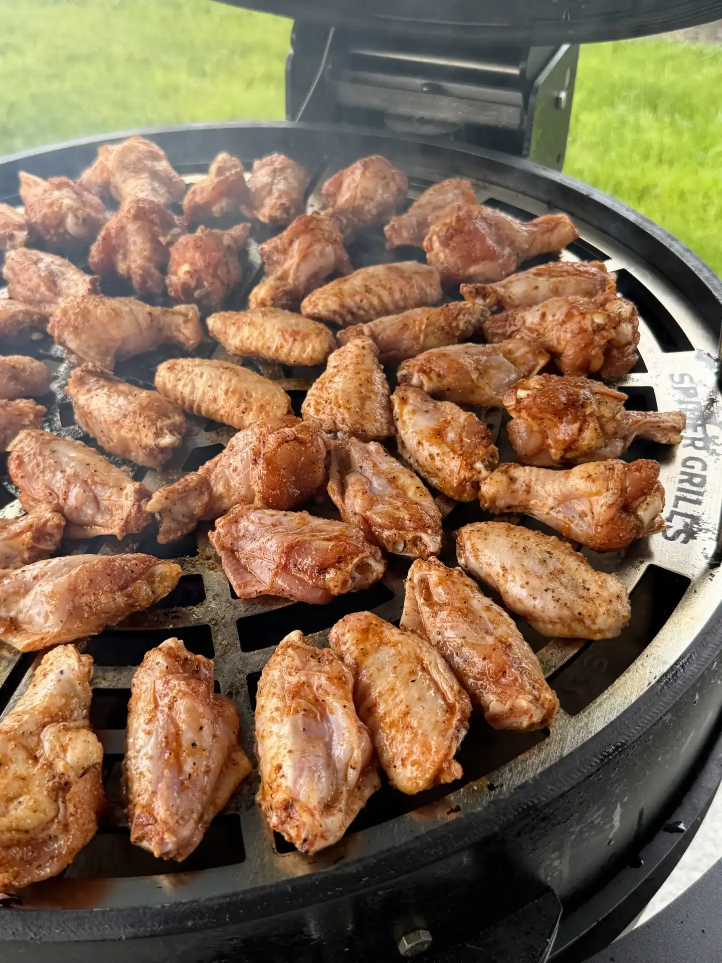 Chicken wings cooking on a round barbecue grill with golden-brown seasoned coating.