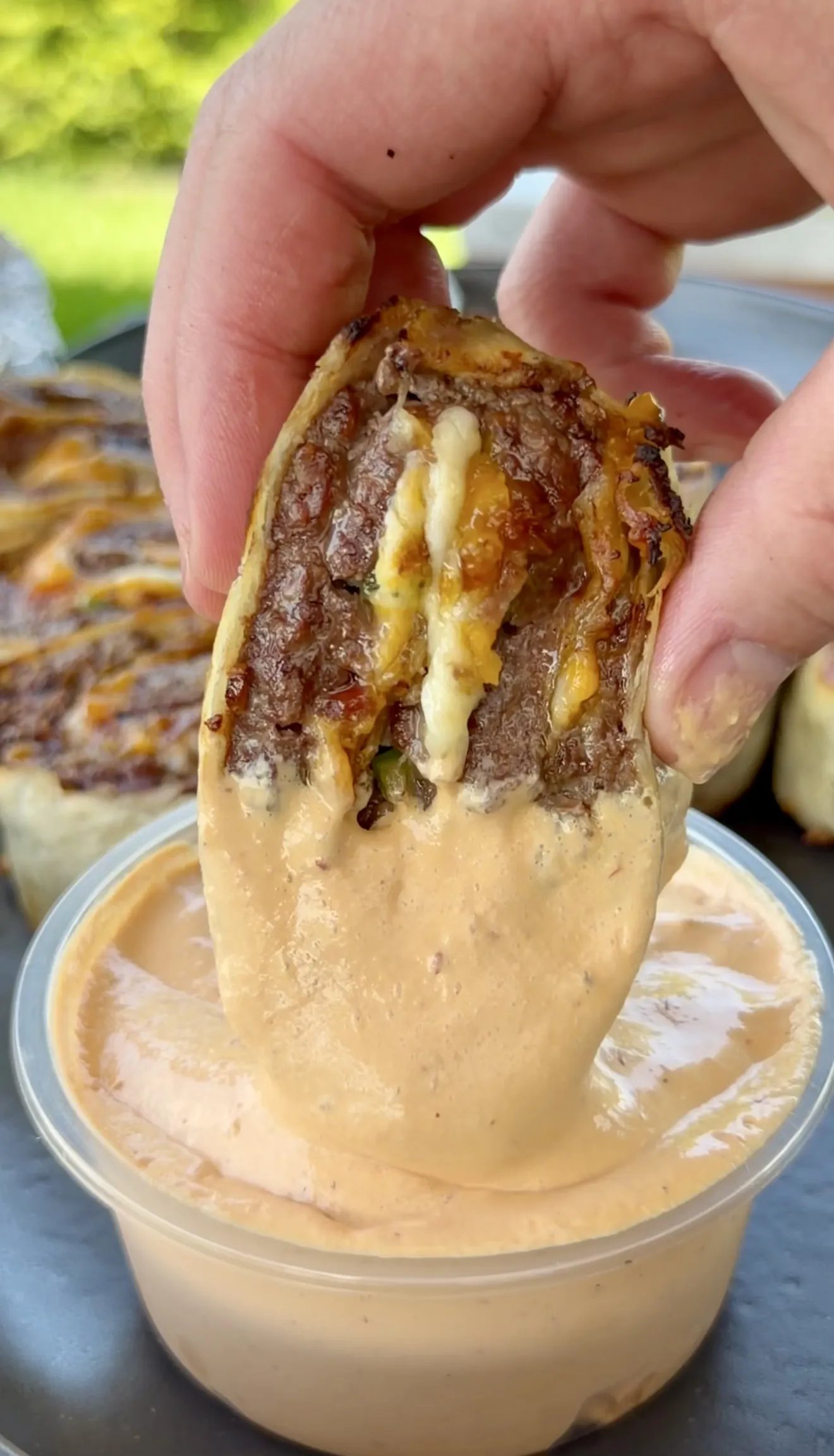 Hand dipping a crispy jalapeño bacon beef pinwheel into chipotle crema