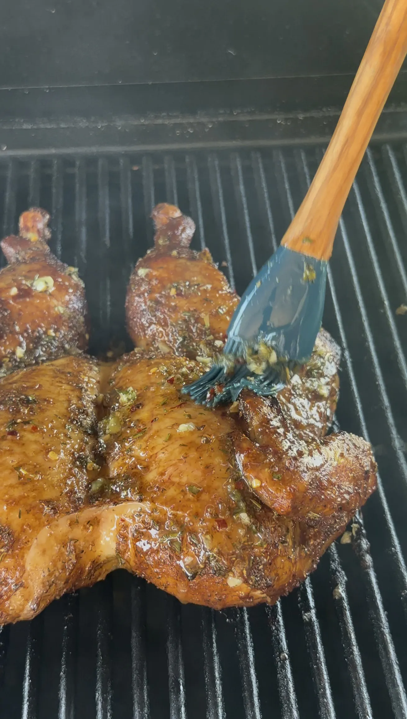 Basting the spatchcock chicken with melted lemon garlic herb butter on the grill