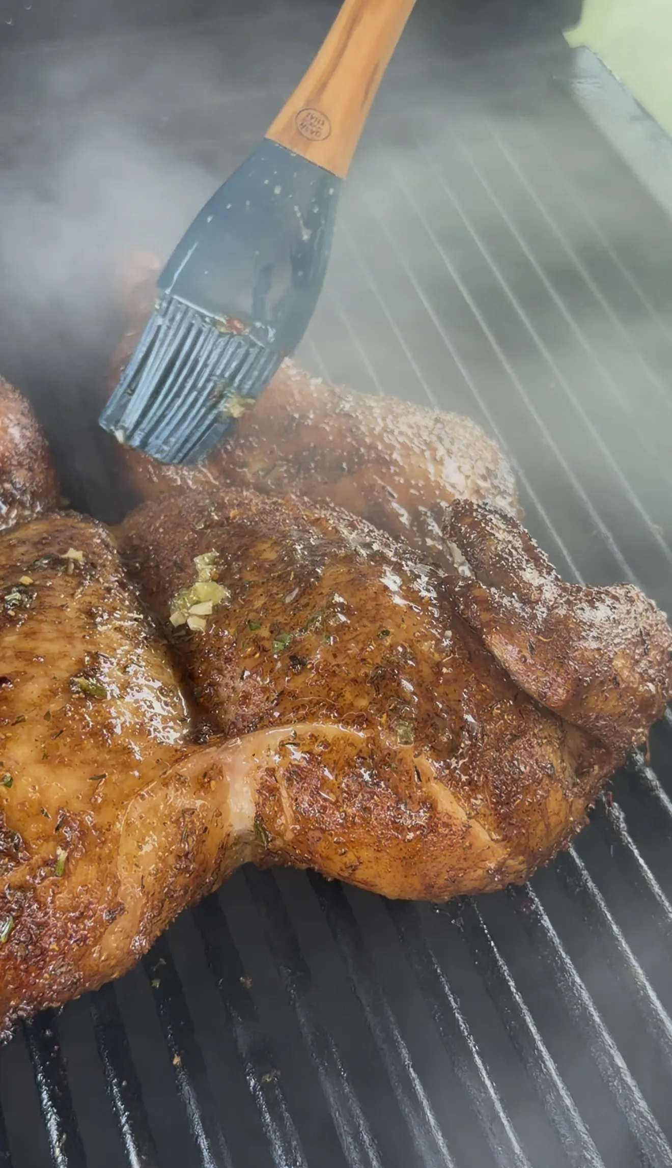 Brushing lemon garlic herb butter over the grilled spatchcock chicken
