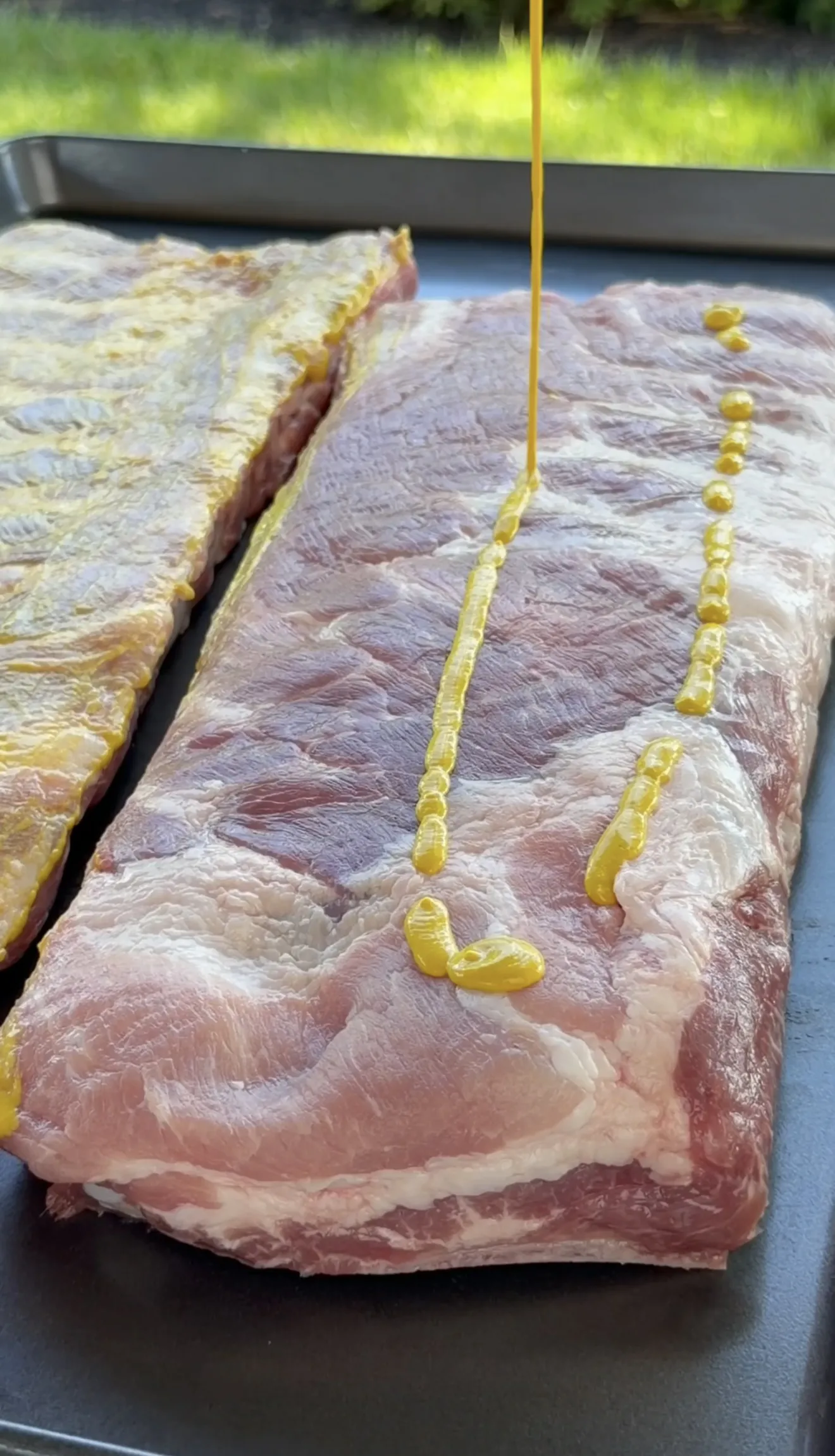 Yellow mustard binder being drizzled onto raw pork spare ribs