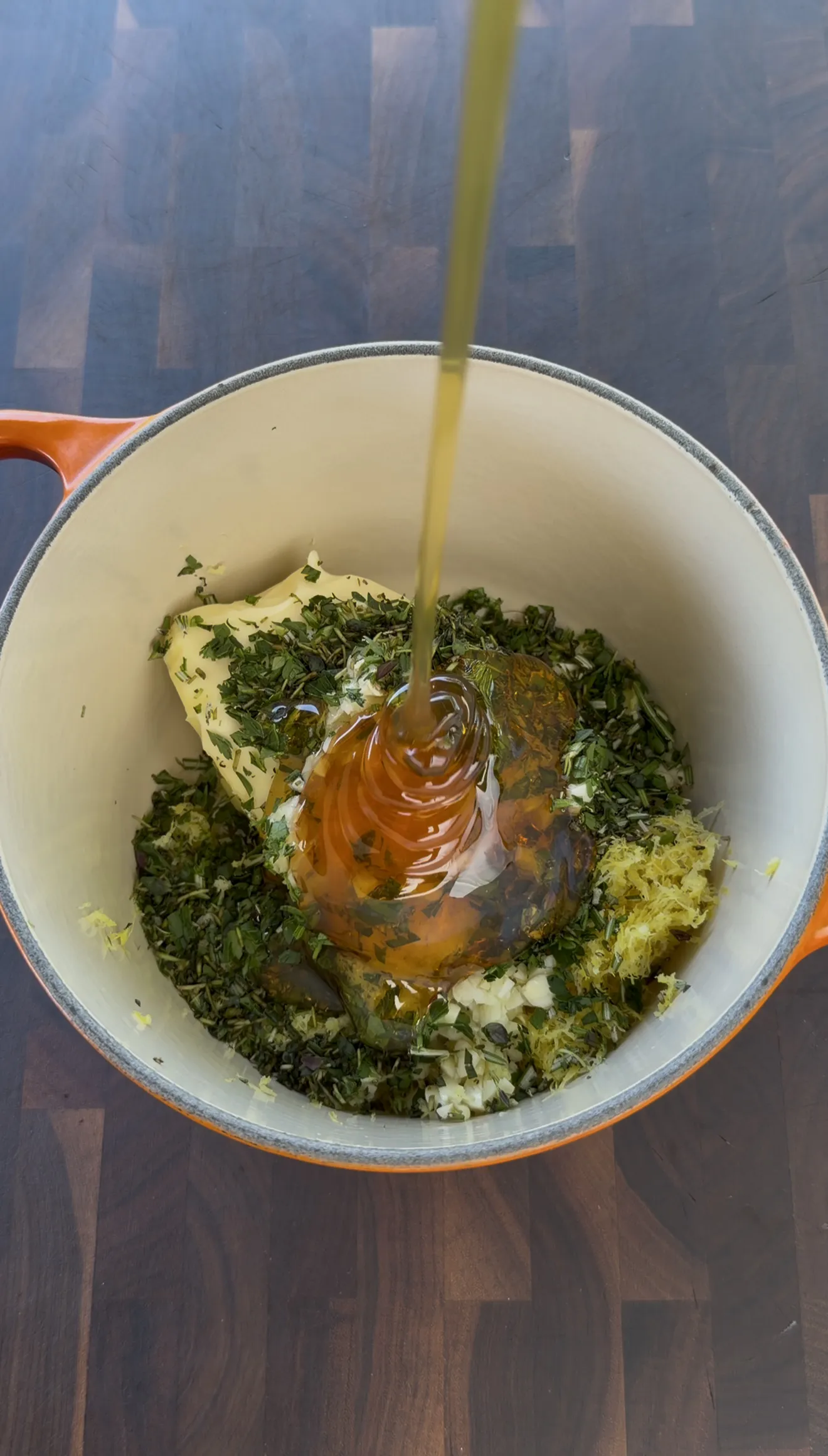 Adding olive oil to the bowl of lemon garlic herb compound butter ingredients