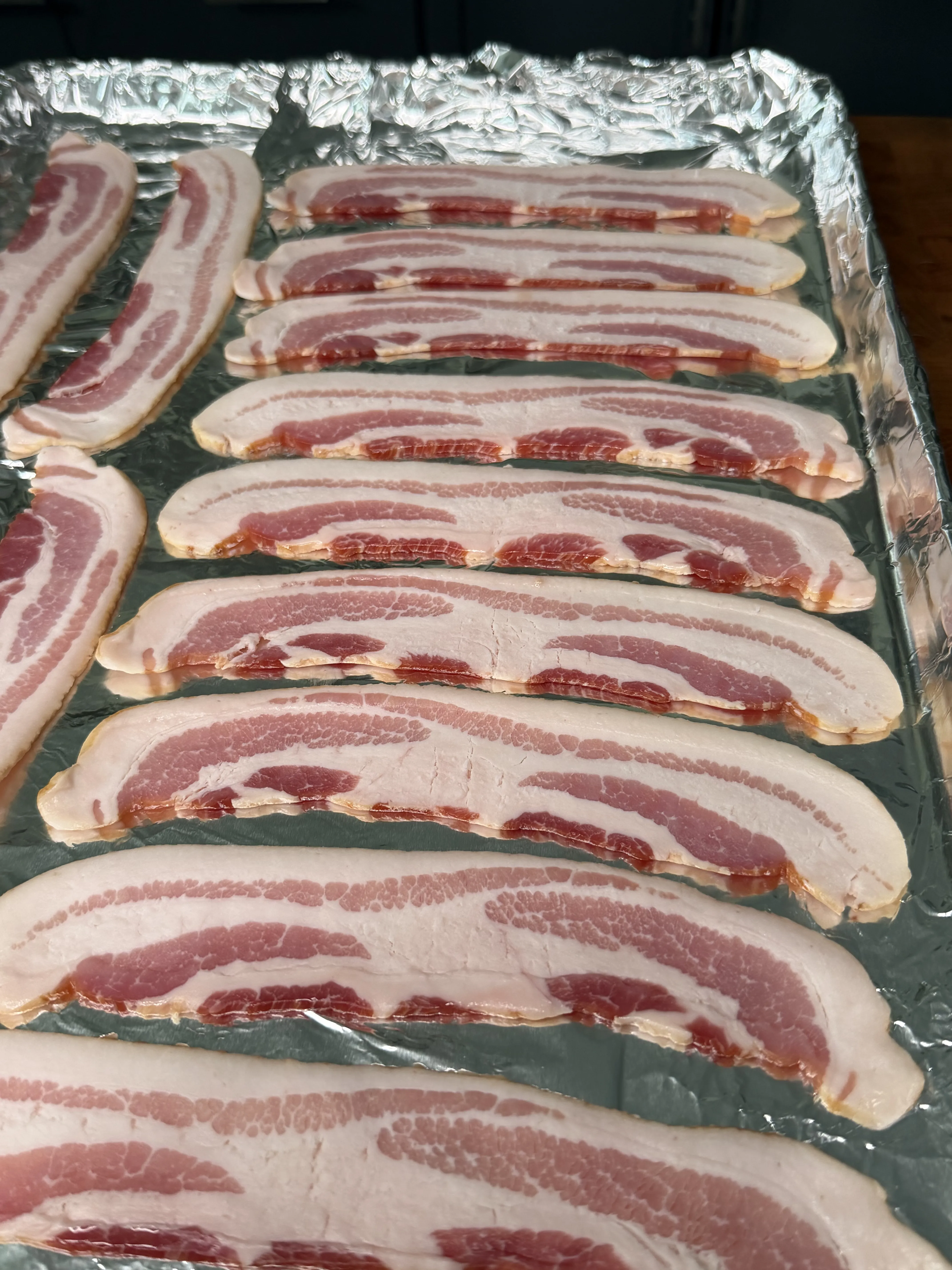 Raw bacon strips on a foil-lined baking sheet ready to cook