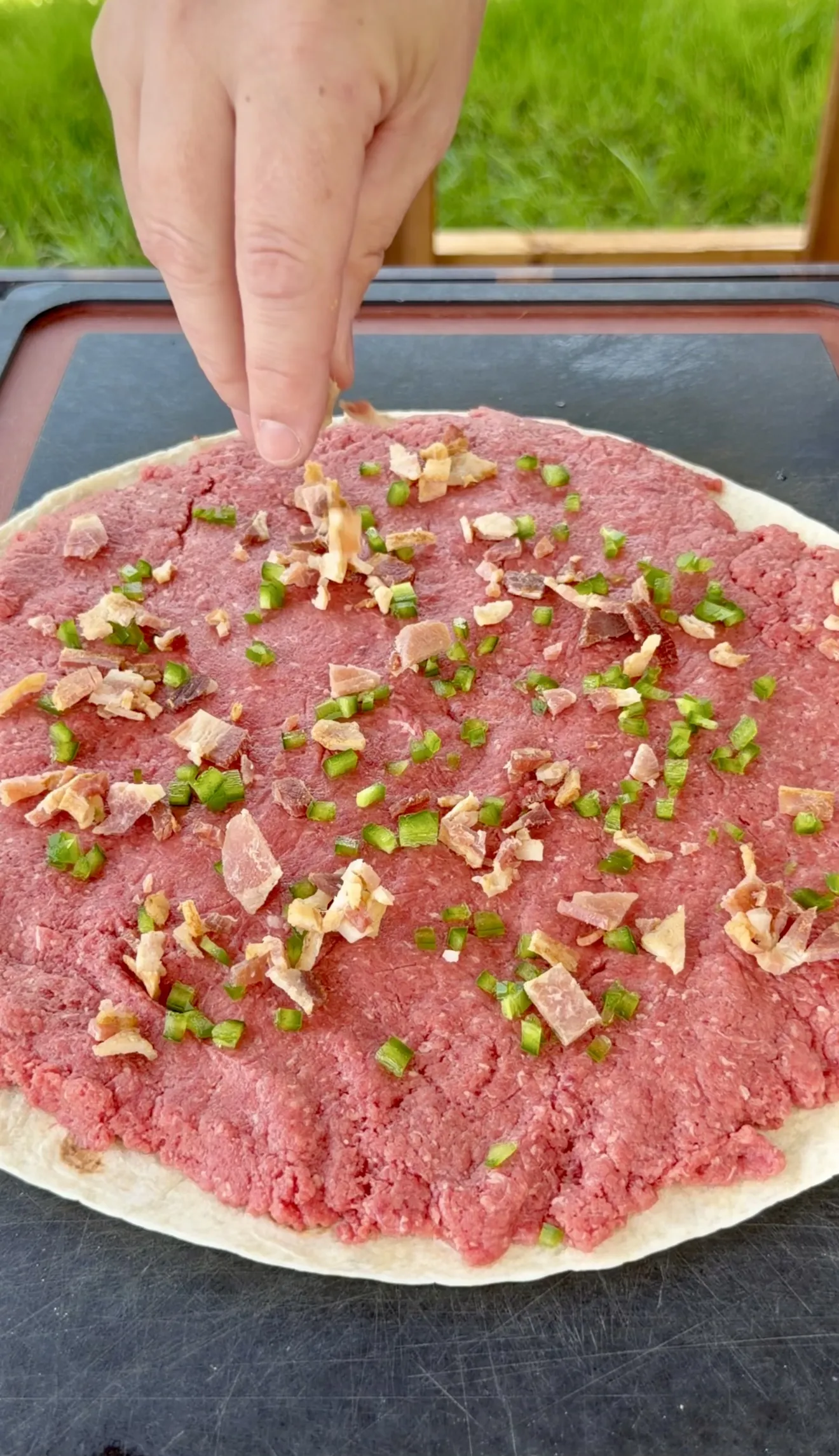 Raw ground beef mixture topped with diced bacon and jalapeños on a tortilla