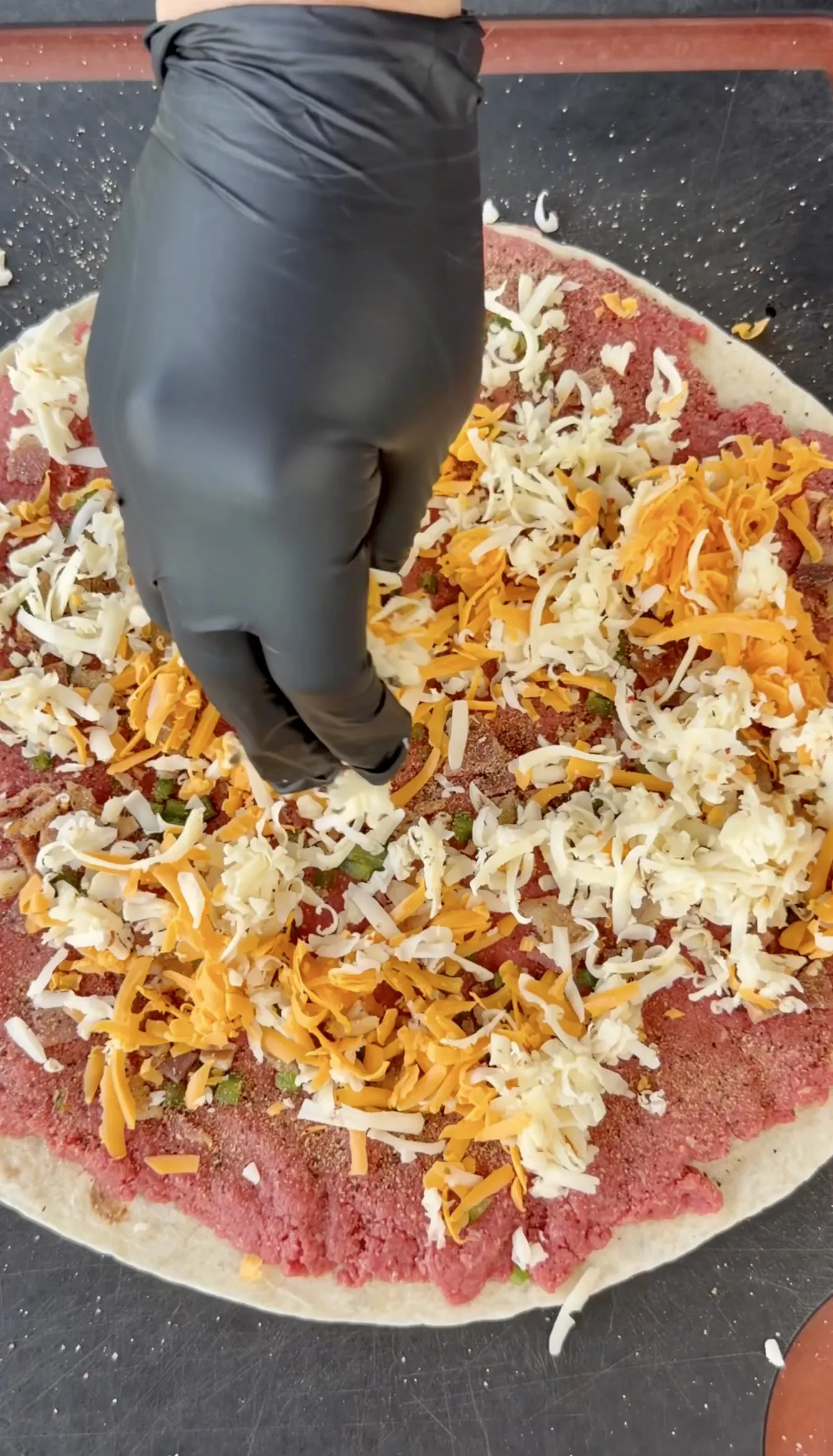 Raw ground beef mixture with shredded cheese spread on a tortilla