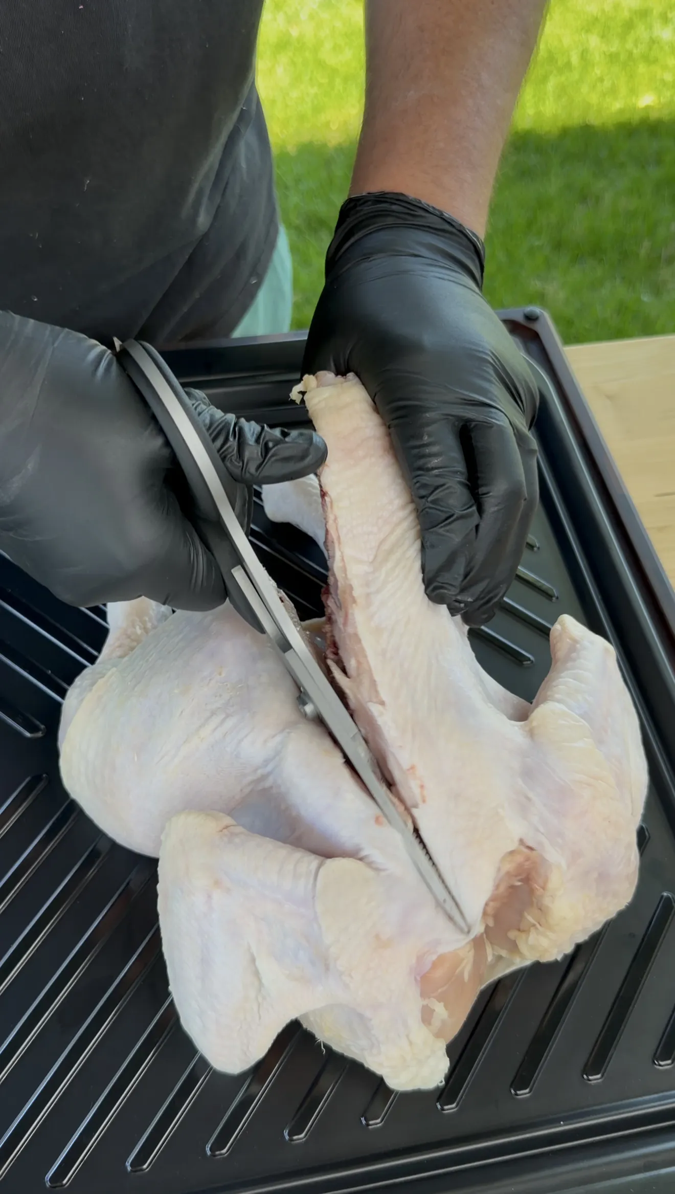 Using poultry shears to cut along the backbone of a whole chicken for spatchcocking