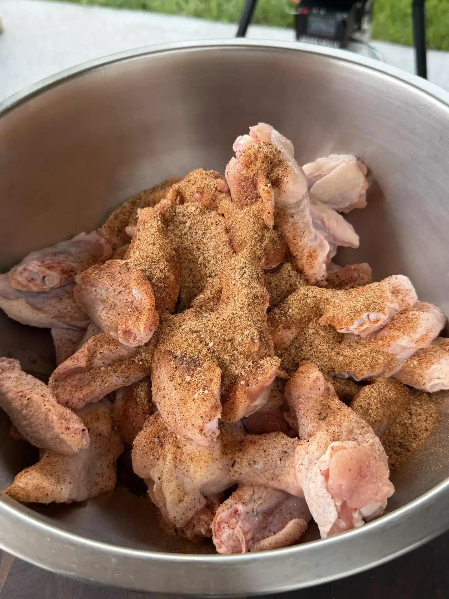 Raw chicken wings coated in lemon pepper seasoning in a stainless steel bowl ready for cooking.