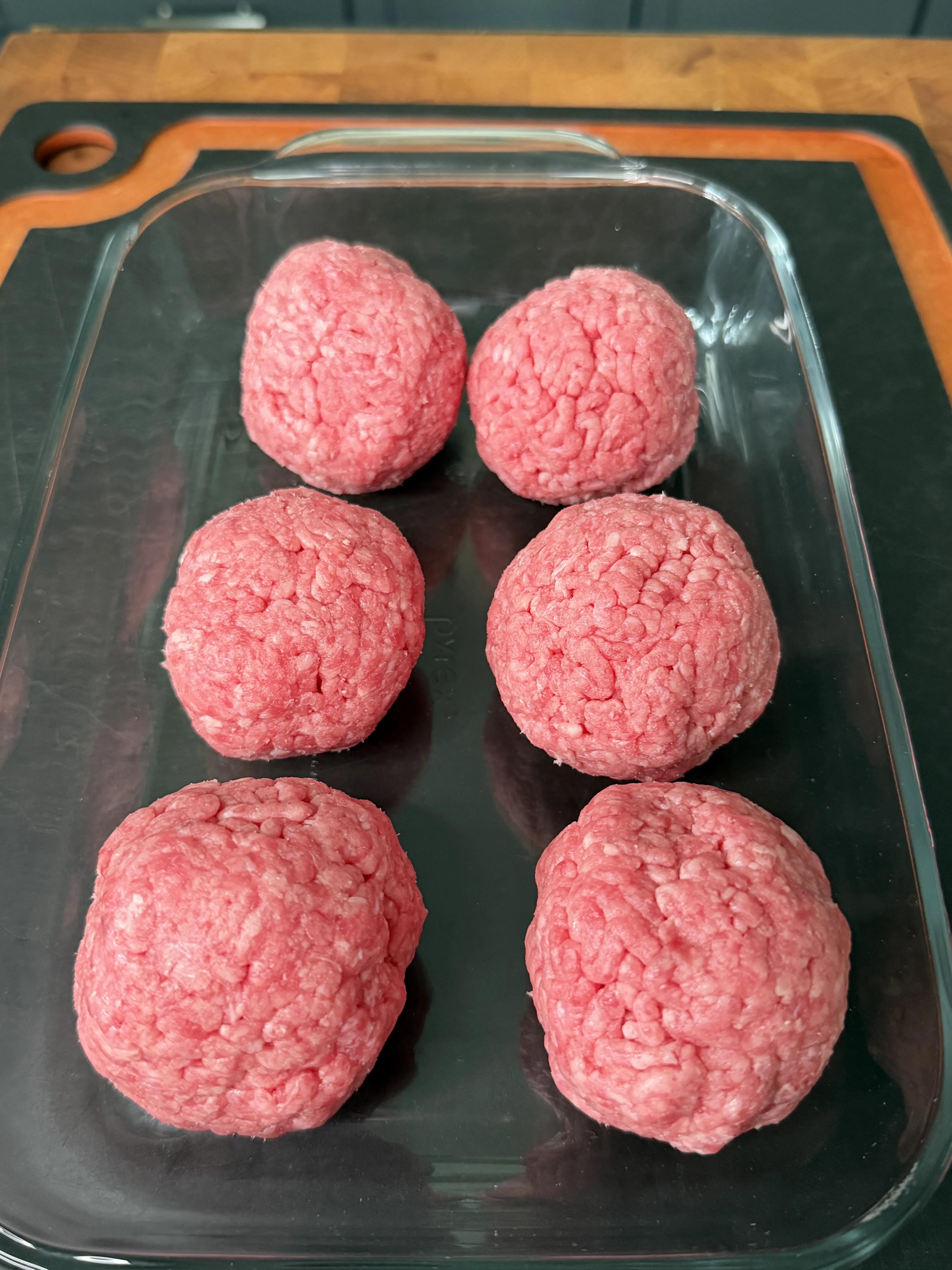 Loosely packed raw 80/20 ground beef balls portioned in a glass dish for the sliders