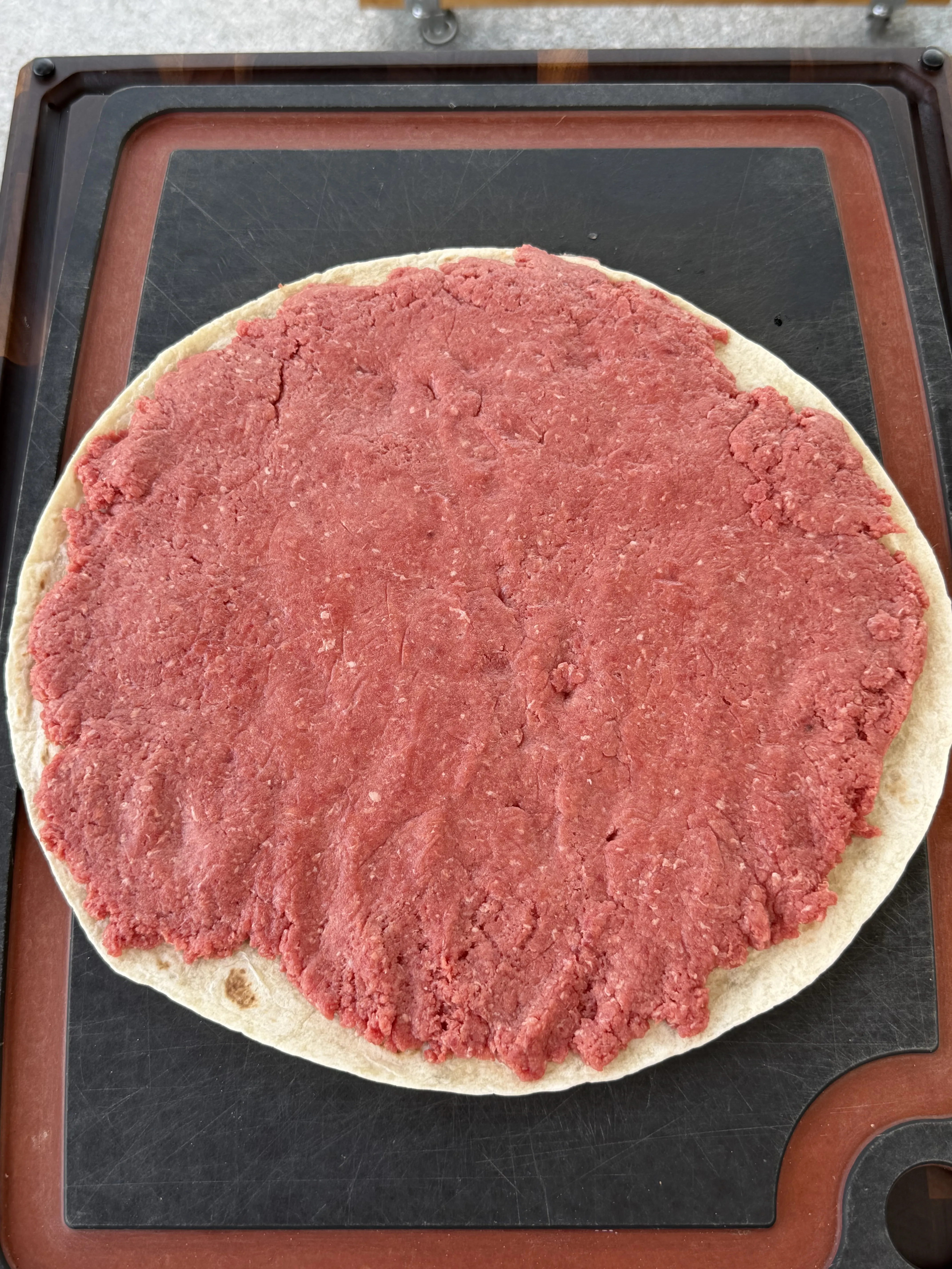 Raw ground beef mixture spread evenly on a flour tortilla for beef pinwheels