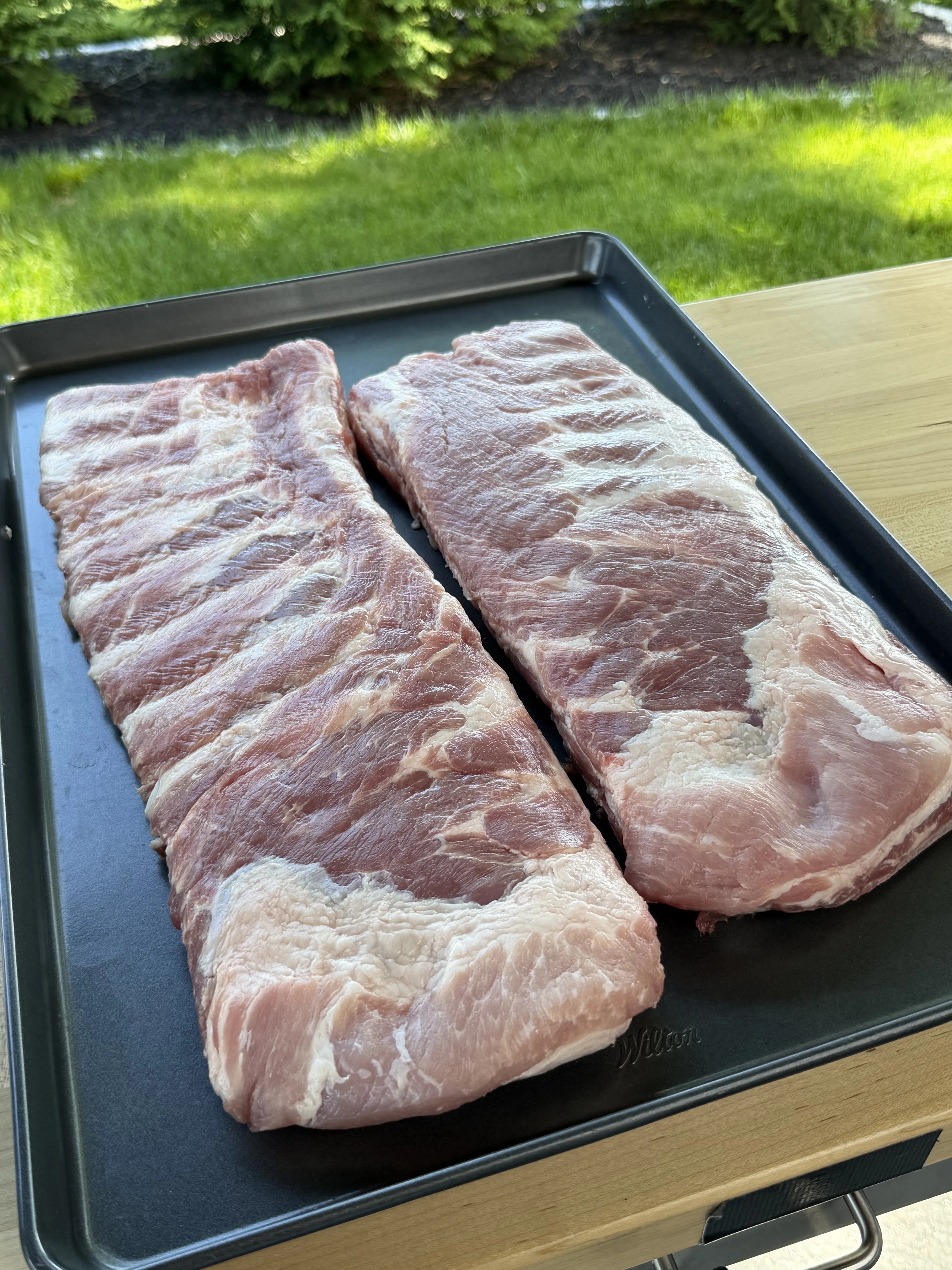 Two racks of raw St. Louis cut pork spare ribs on a baking sheet ready for competition smoking