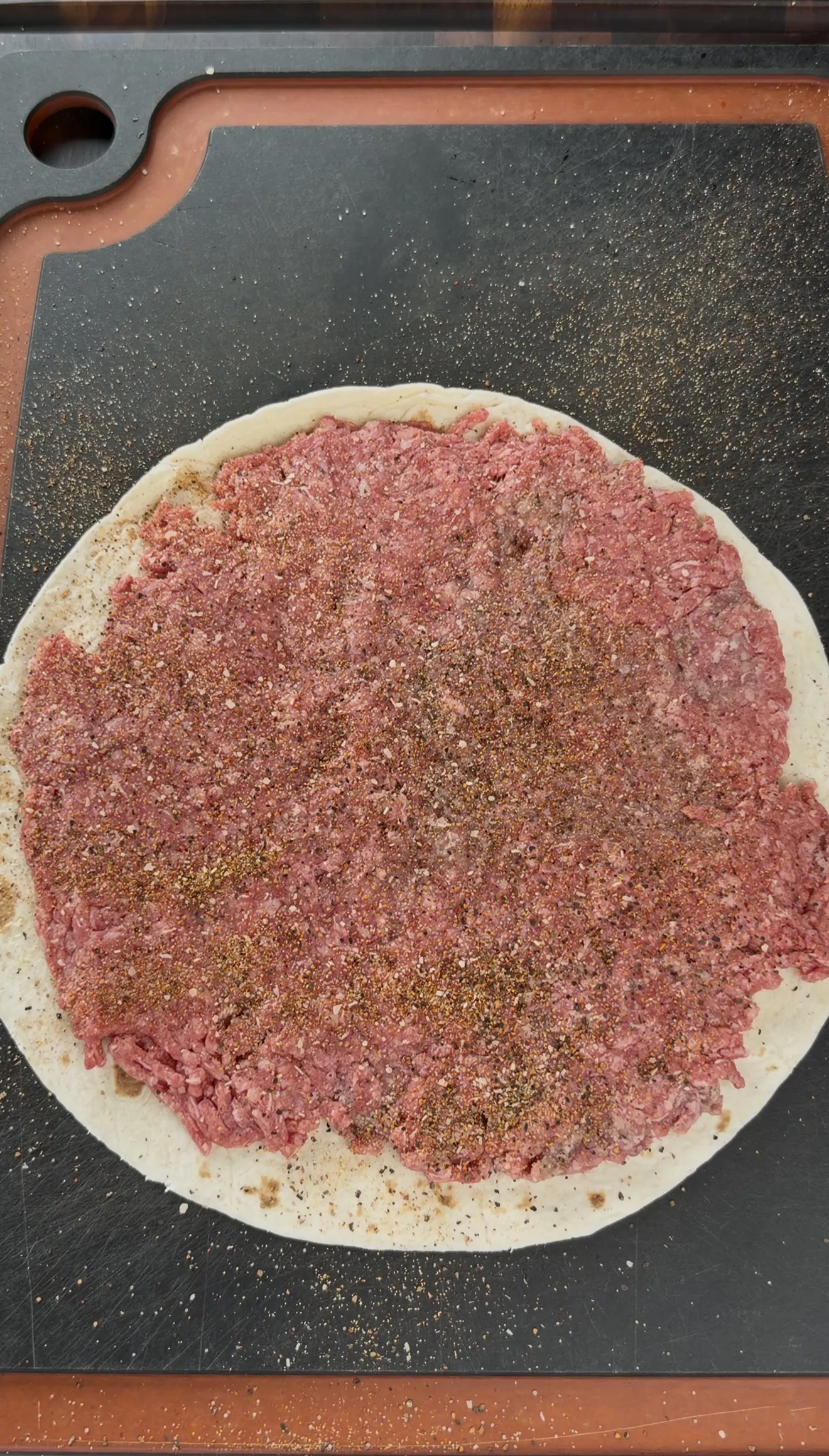 Raw seasoned ground beef spread evenly over a flour tortilla ready for rolling