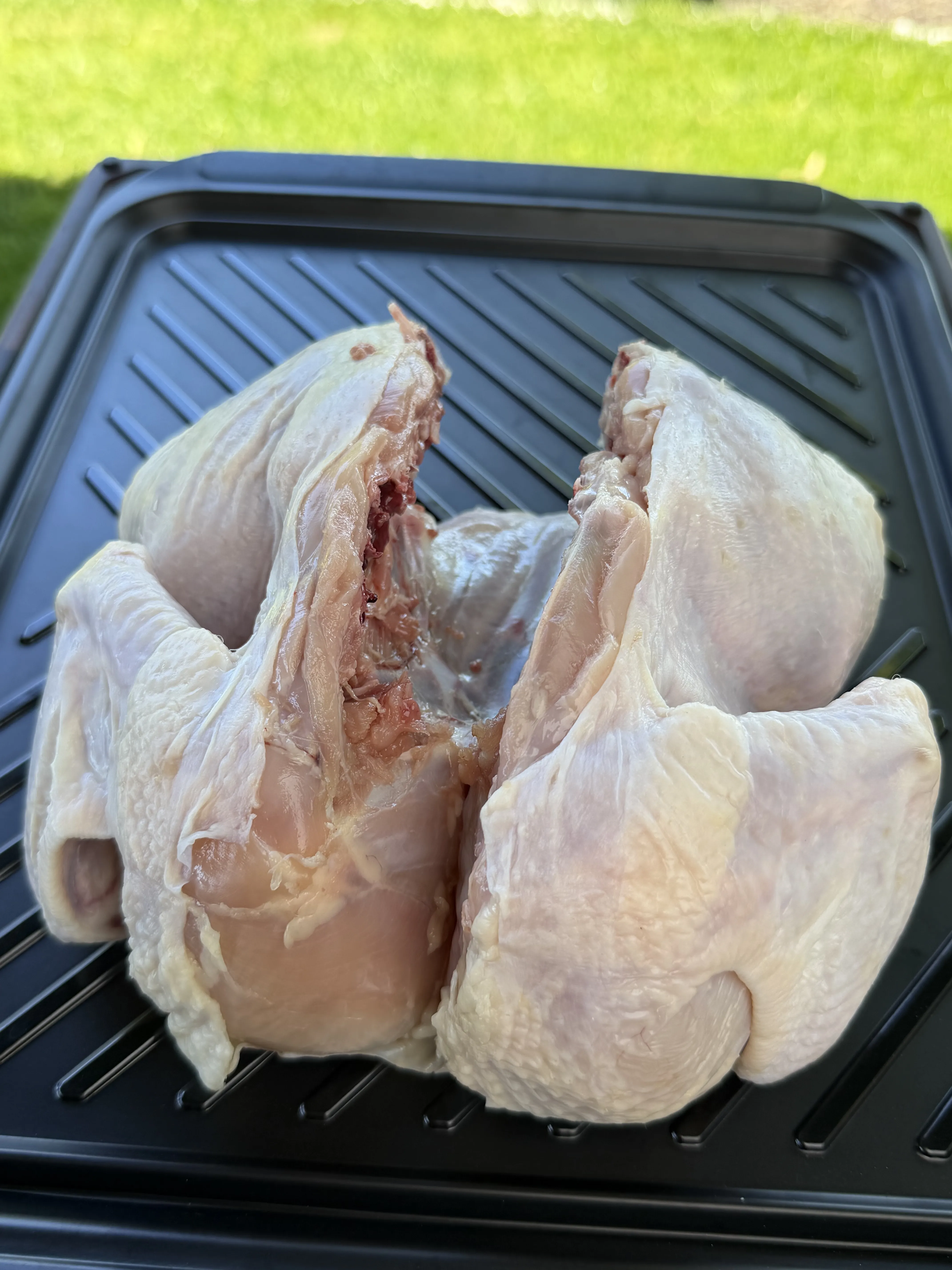 Raw spatchcocked chicken pressed flat on a grill pan ready for seasoning