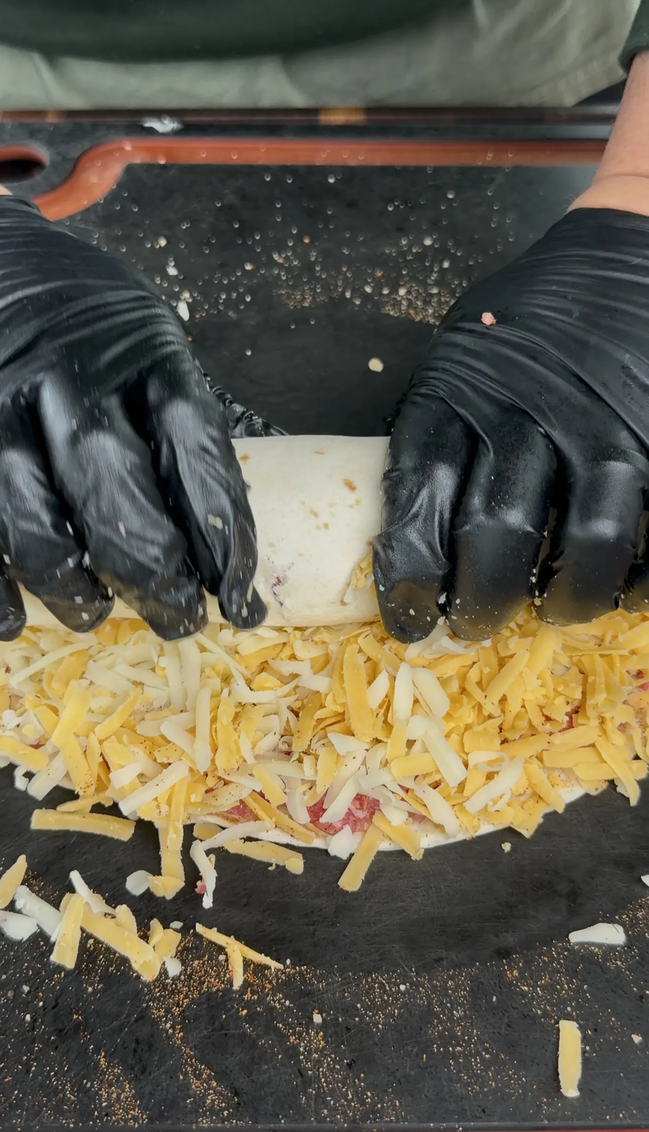 Rolling a cowboy butter beef tortilla pinwheel through shredded cheese