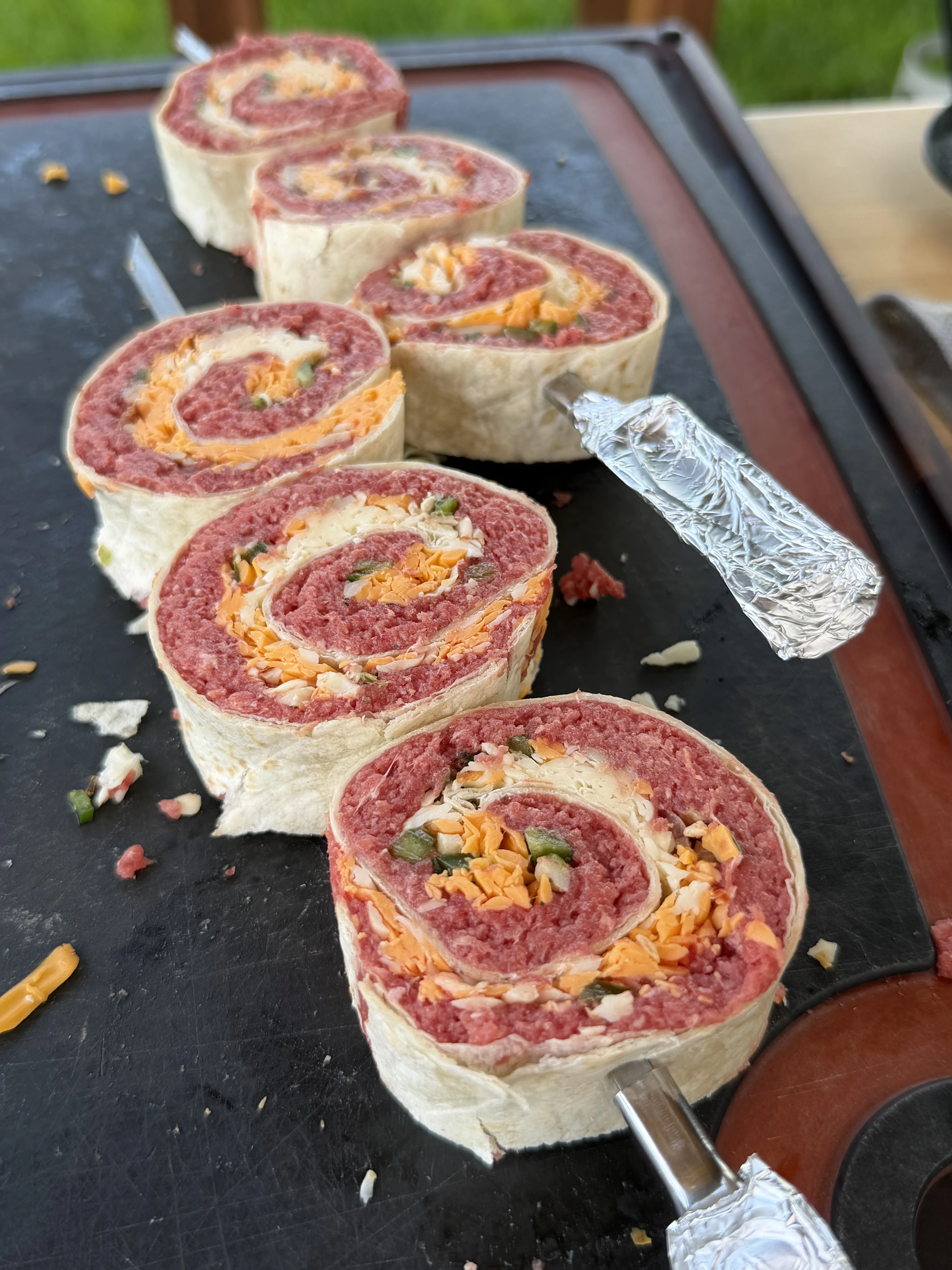 Six sliced beef pinwheels with jalapeño bacon filling on a dark slate serving board