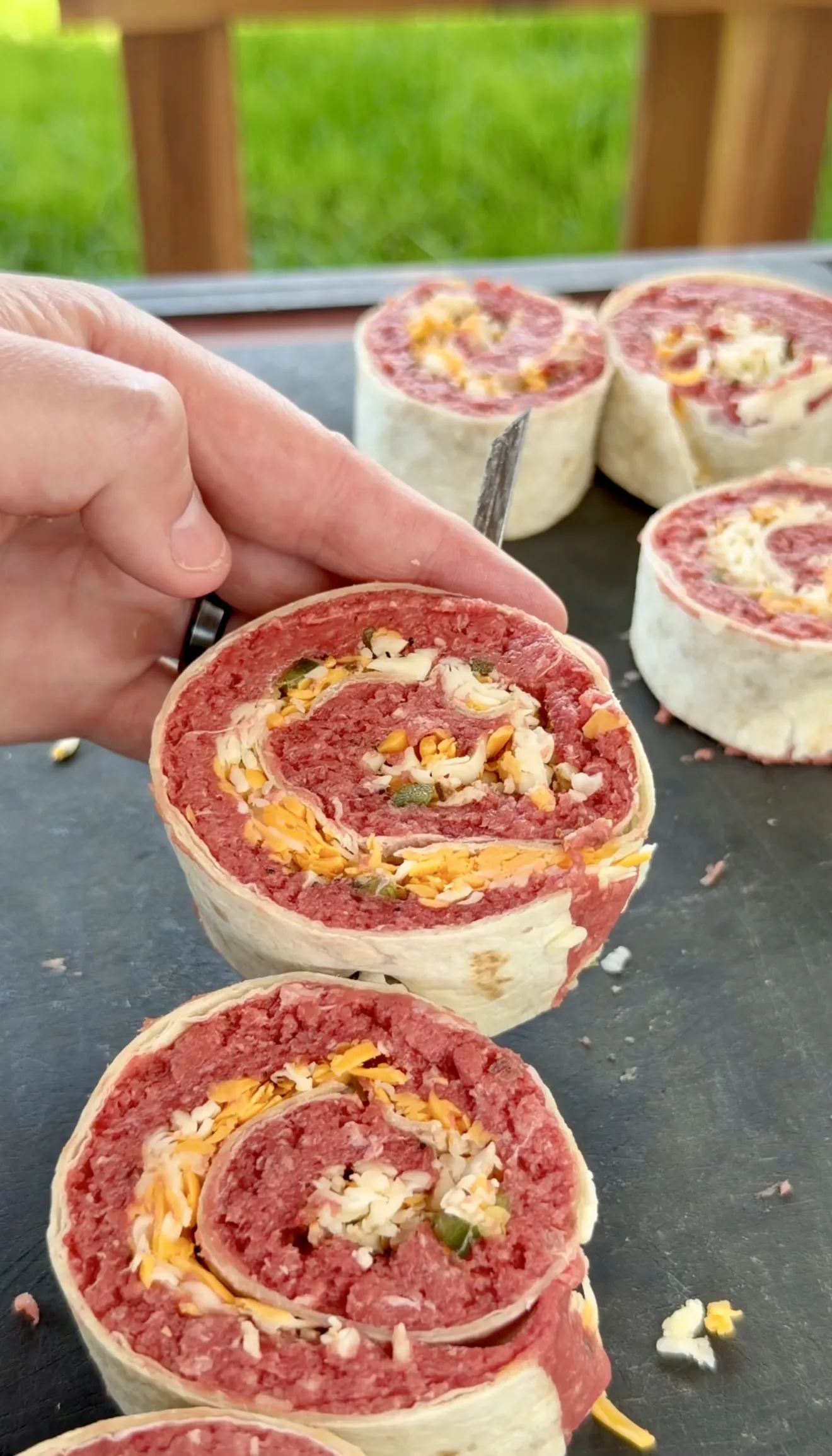 Sliced crispy jalapeño bacon beef pinwheels showing spiral layers on a dark slate board