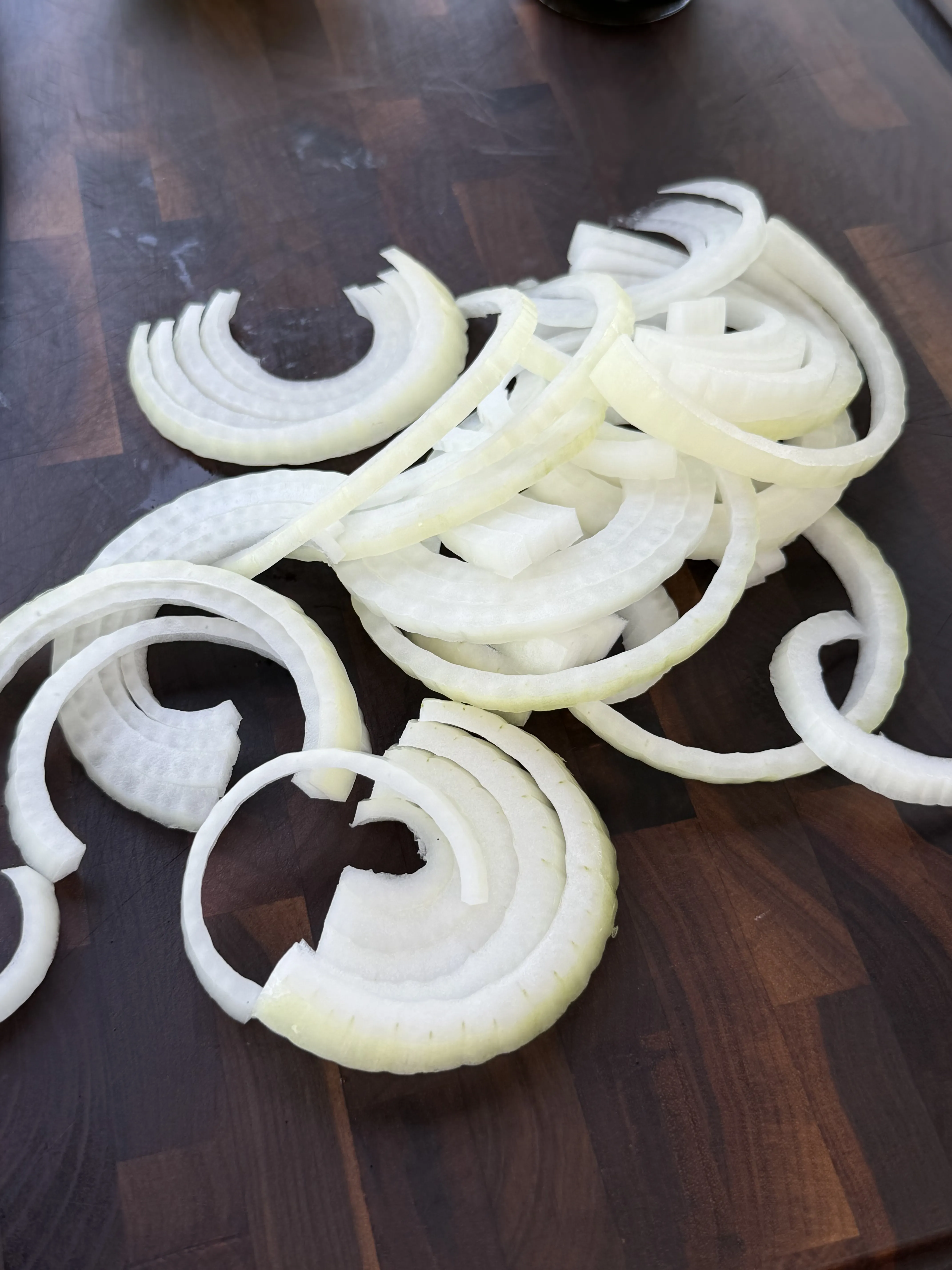 Thinly sliced white onions on a cutting board for caramelizing