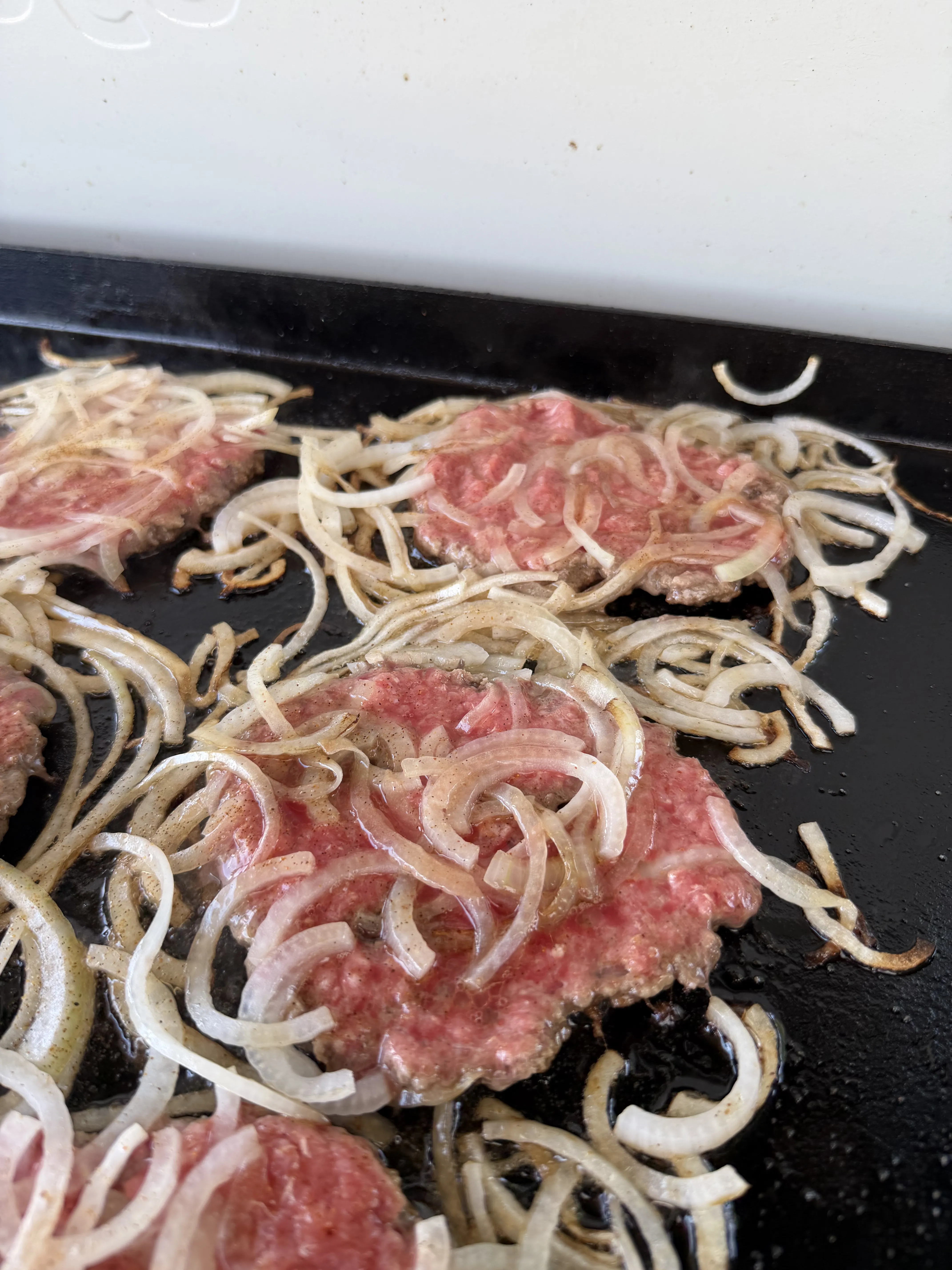 Smash burger patties with onions cooking on a flat-top griddle