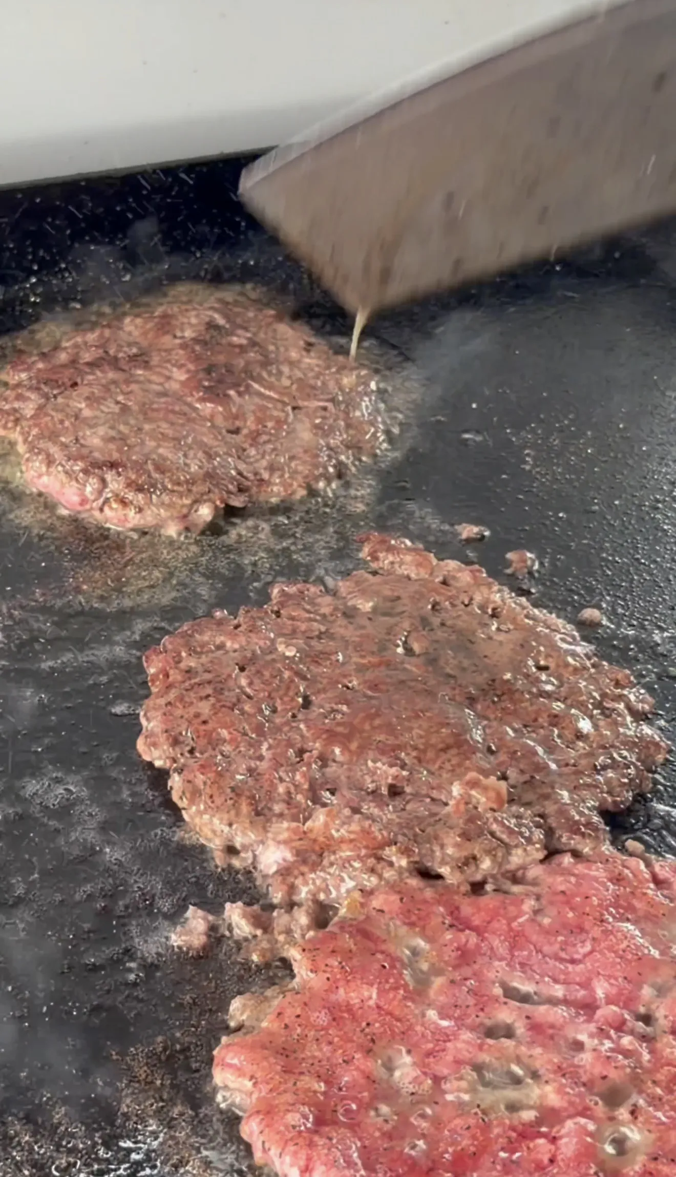 Smashed beef burger patties cooking on a hot flat top griddle
