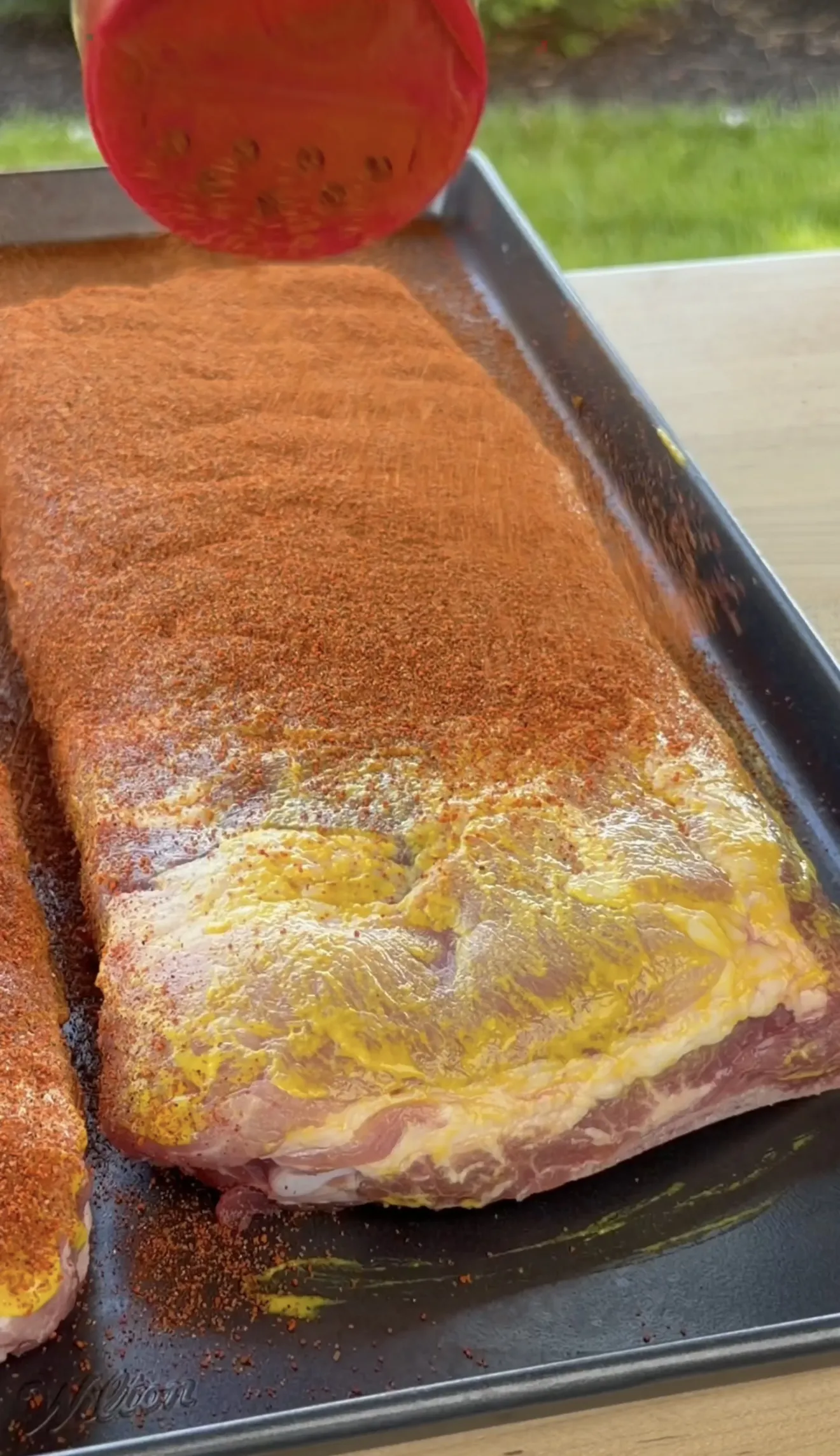 Raw spare ribs coated with yellow mustard binder and red competition dry rub