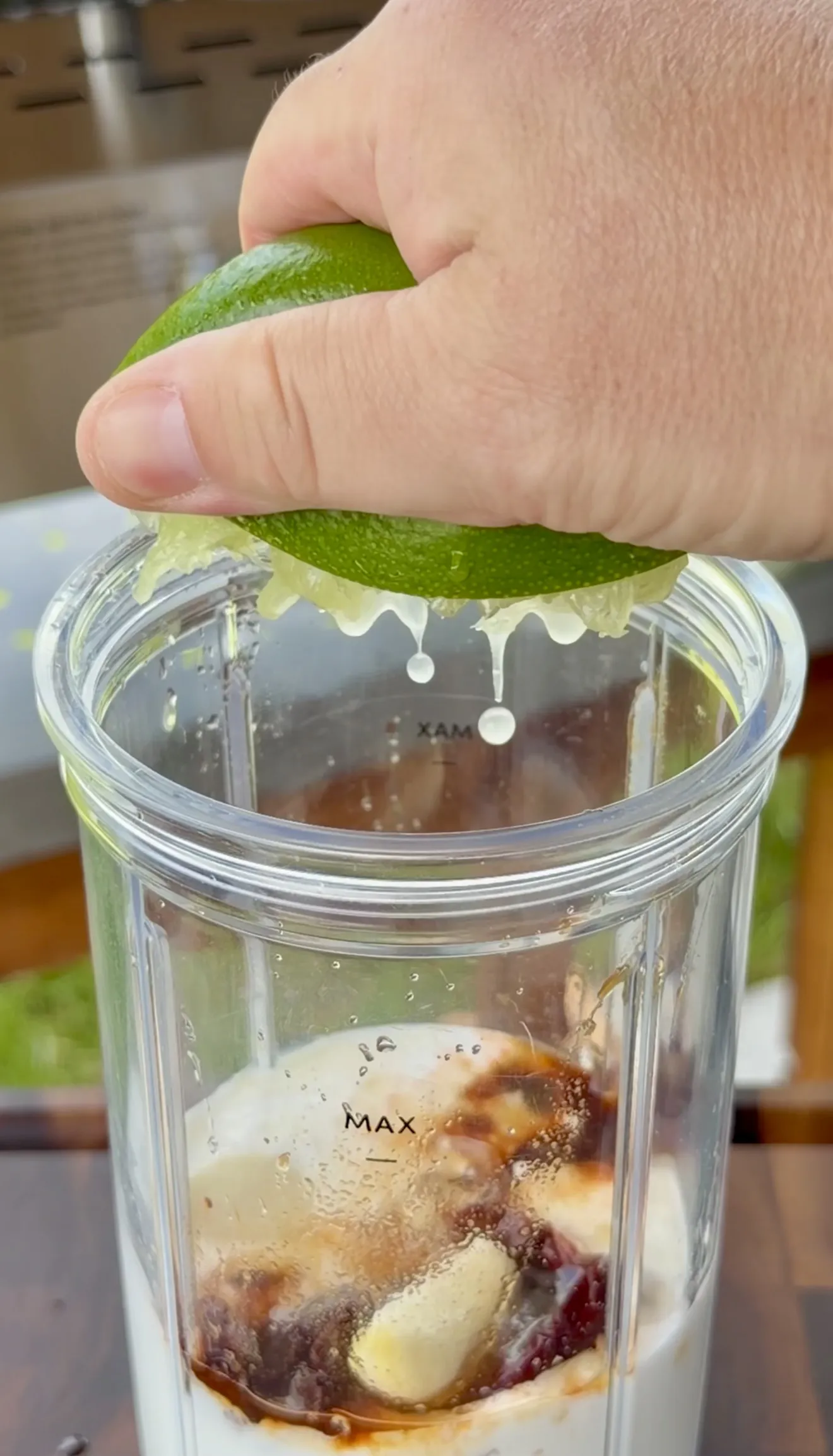 Hand squeezing fresh lime juice into a glass blender with chipotle crema ingredients