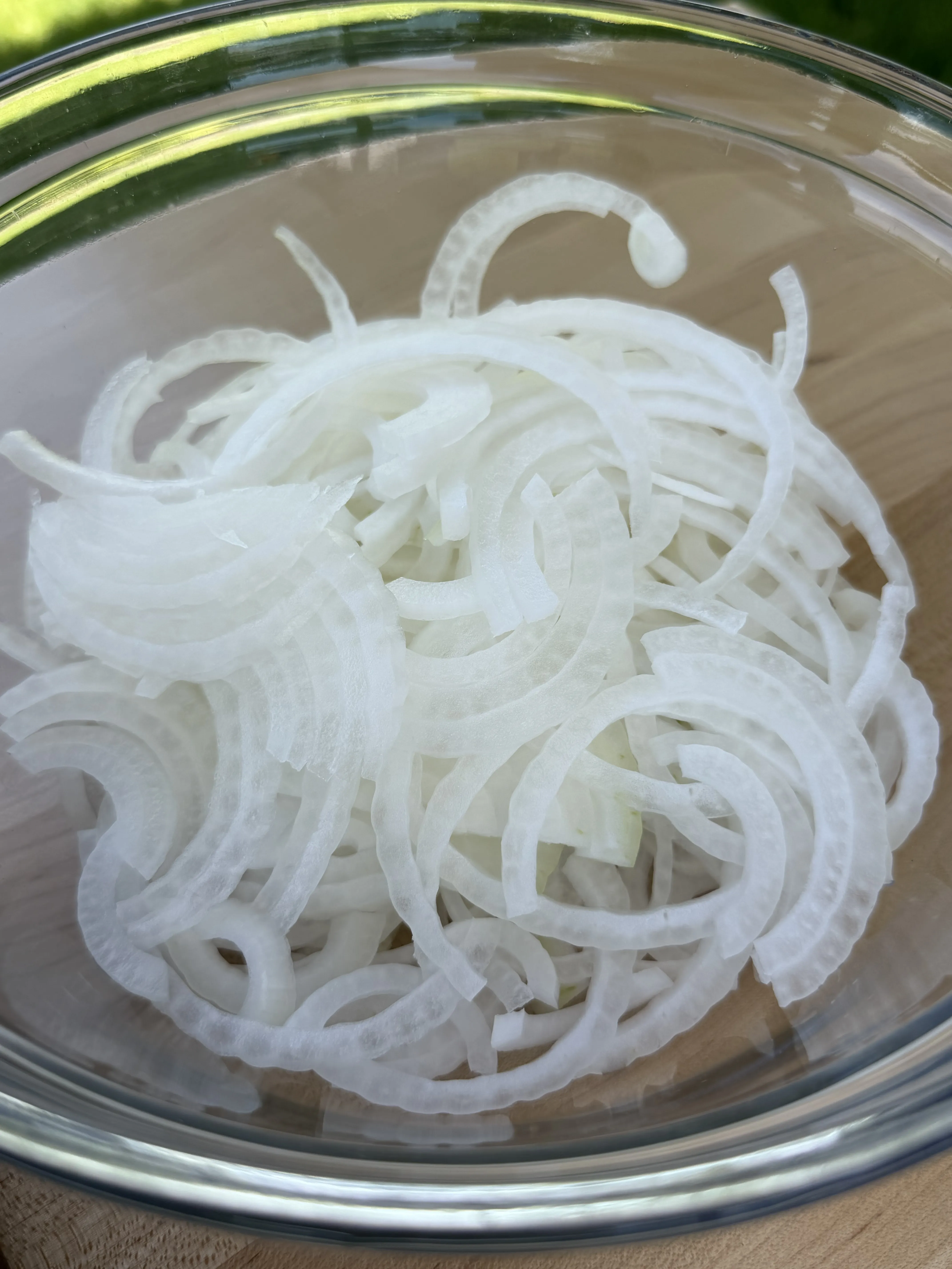 Thinly sliced white onions in a glass bowl ready to smash into the burgers