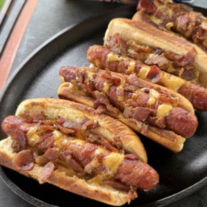 Baconnaise loaded hot dogs topped with crispy bacon and melted cheese sauce served in toasted buns on a cast iron skillet