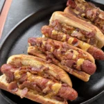 Baconnaise loaded hot dogs topped with crispy bacon and melted cheese sauce served in a cast iron skillet