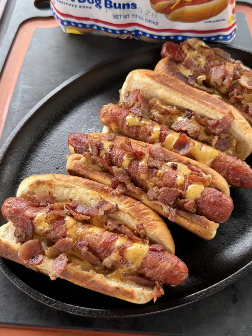 Baconnaise loaded hot dogs topped with crispy bacon and melted cheese sauce served in a cast iron skillet