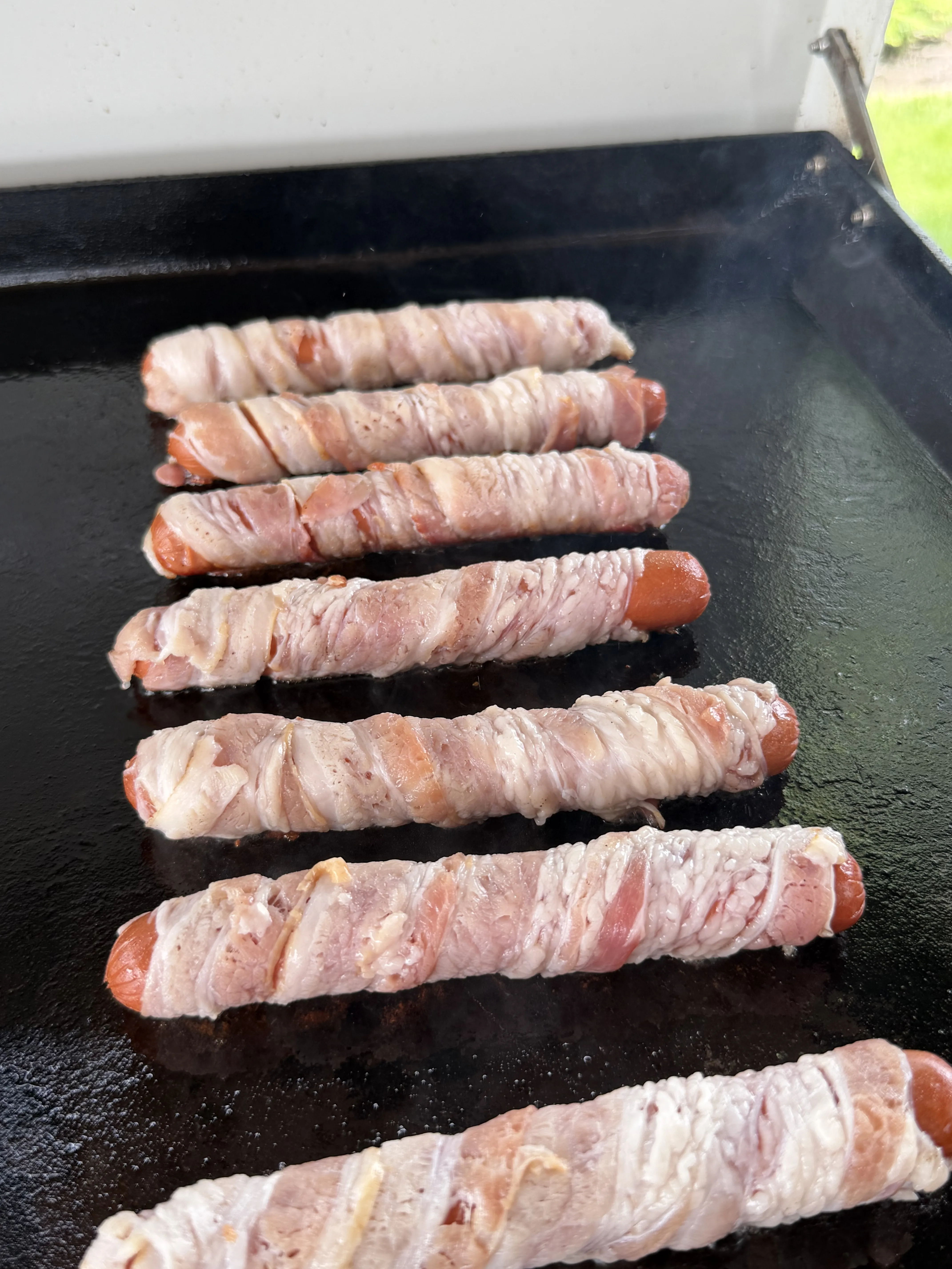 Bacon wrapped hot dogs cooking with the bacon spiral-wrapped around each frank
