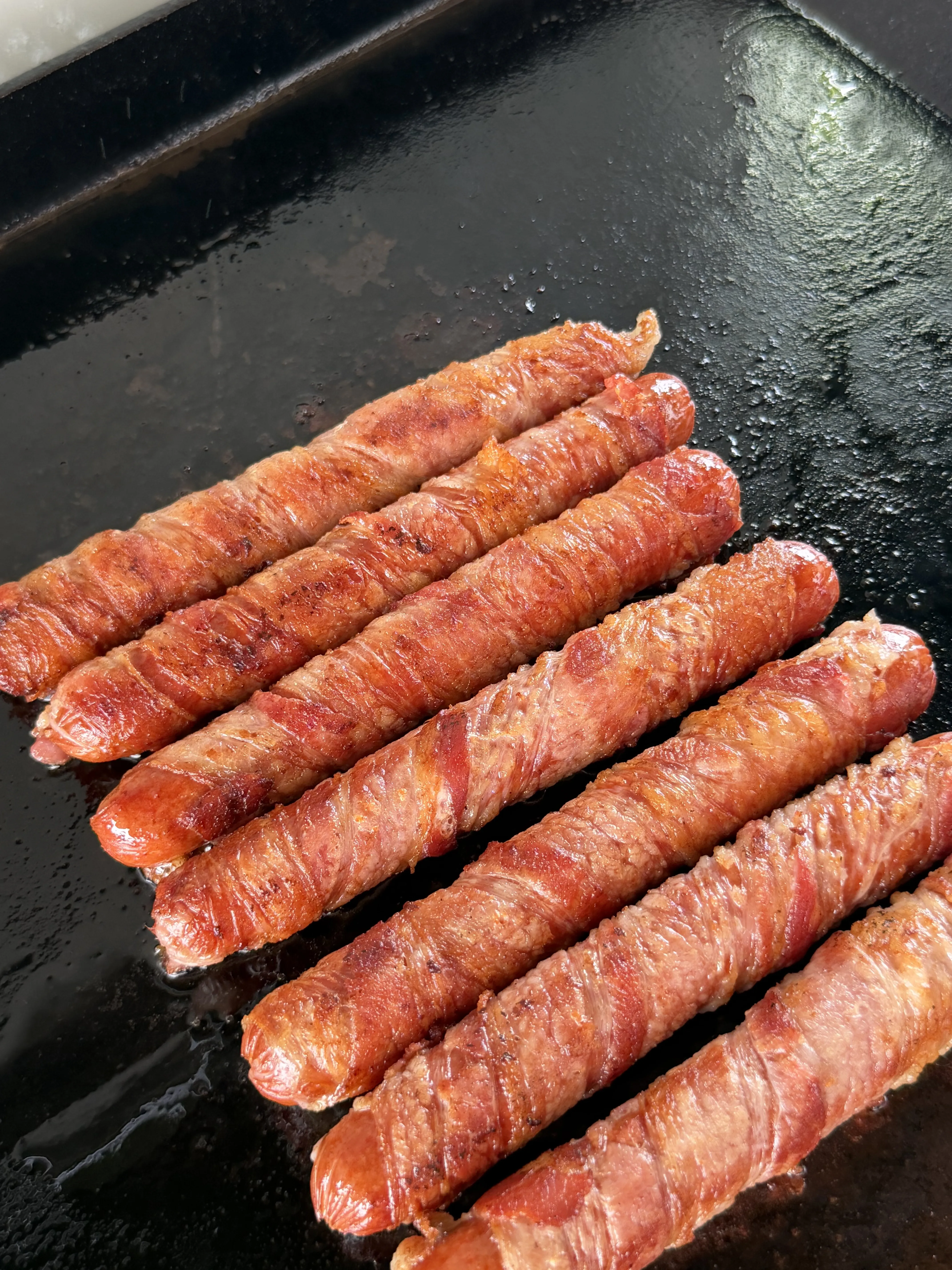 Bacon wrapped hot dogs golden brown and crispy as the bacon renders
