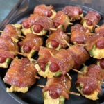 Smoked bacon wrapped jalapeño smokie bombs filled with cream cheese, secured with toothpicks in a cast iron skillet