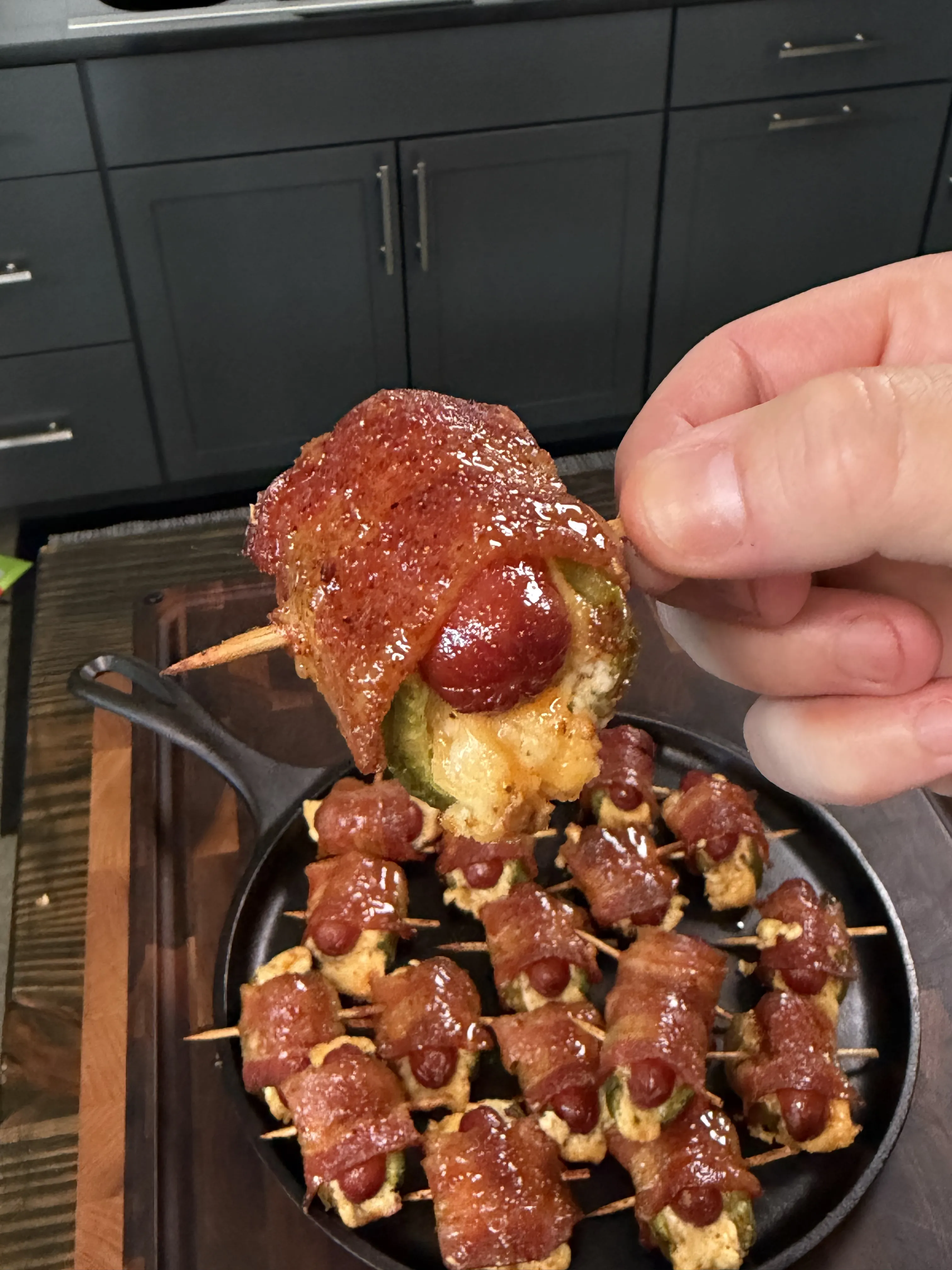 Glazed bacon wrapped jalapeño smokie bomb held over a cast iron skillet of more