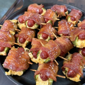 Smoked bacon wrapped jalapeño smokie bombs filled with cream cheese, secured with toothpicks in a cast iron skillet