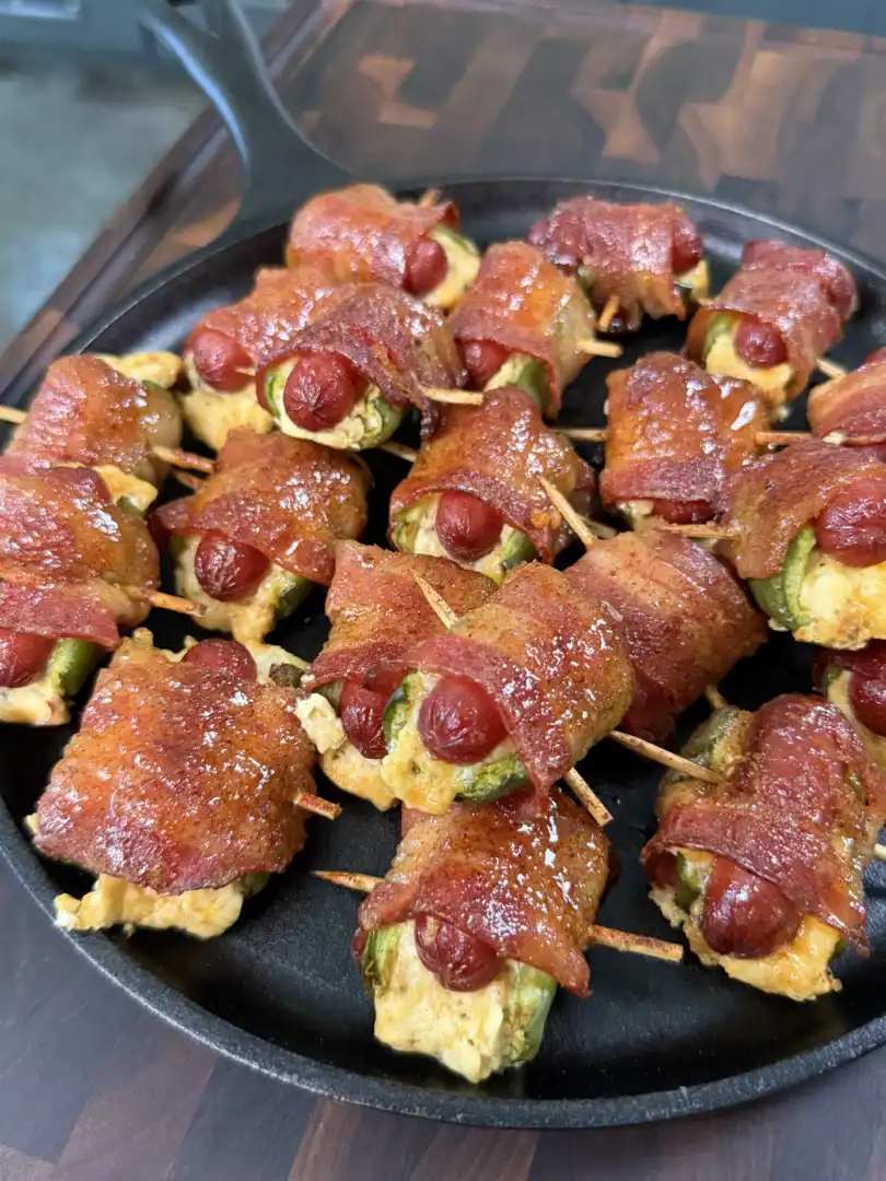 Smoked bacon wrapped jalapeño smokie bombs filled with cream cheese, secured with toothpicks in a cast iron skillet