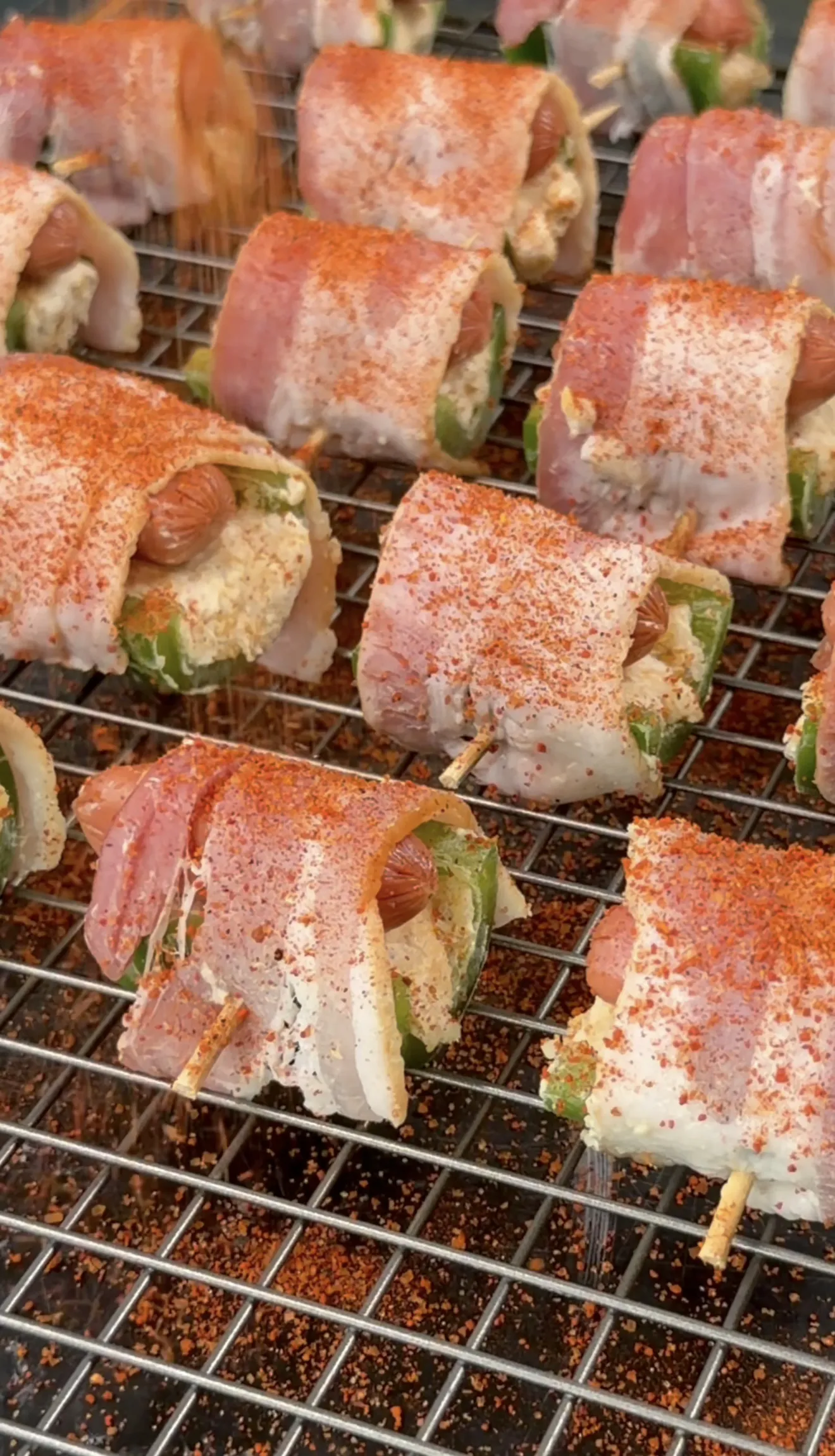 Raw bacon wrapped jalapeño smokie bombs dusted with BBQ rub on a wire rack ready to smoke