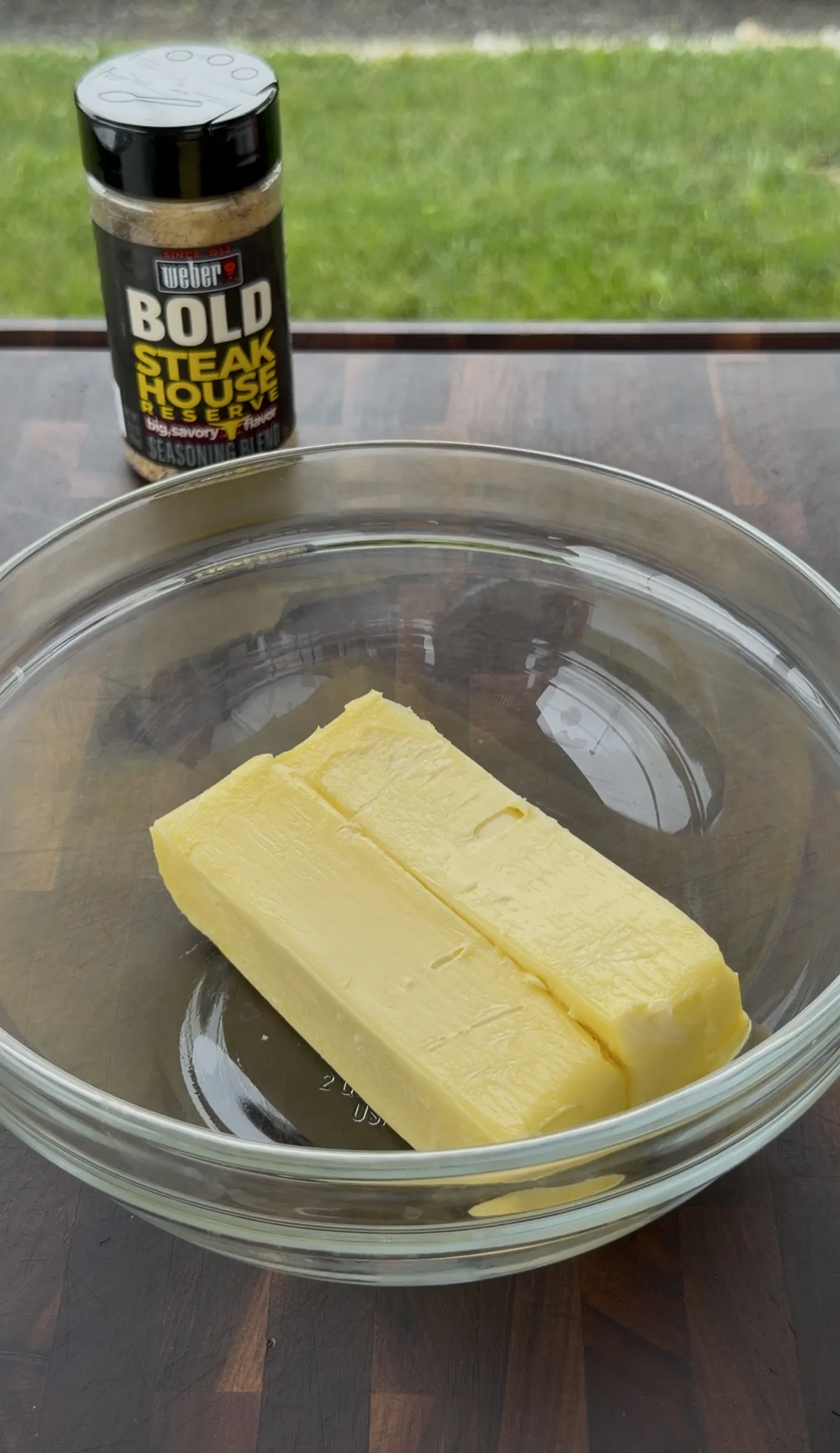 Two sticks of softened butter in a glass bowl next to a steakhouse seasoning blend