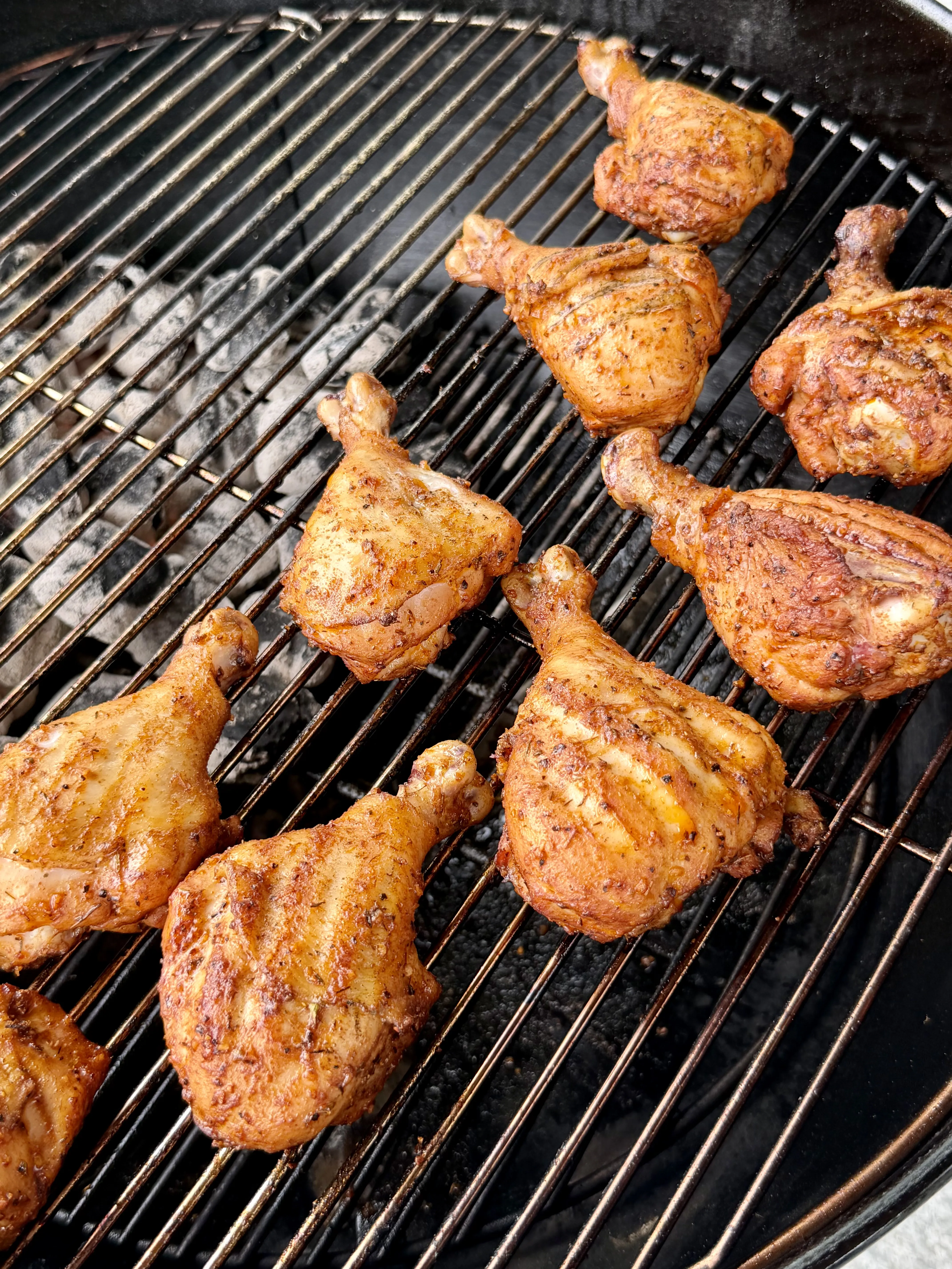 Seasoned Cajun chicken drumsticks and thighs grilling over charcoal on a round BBQ grill