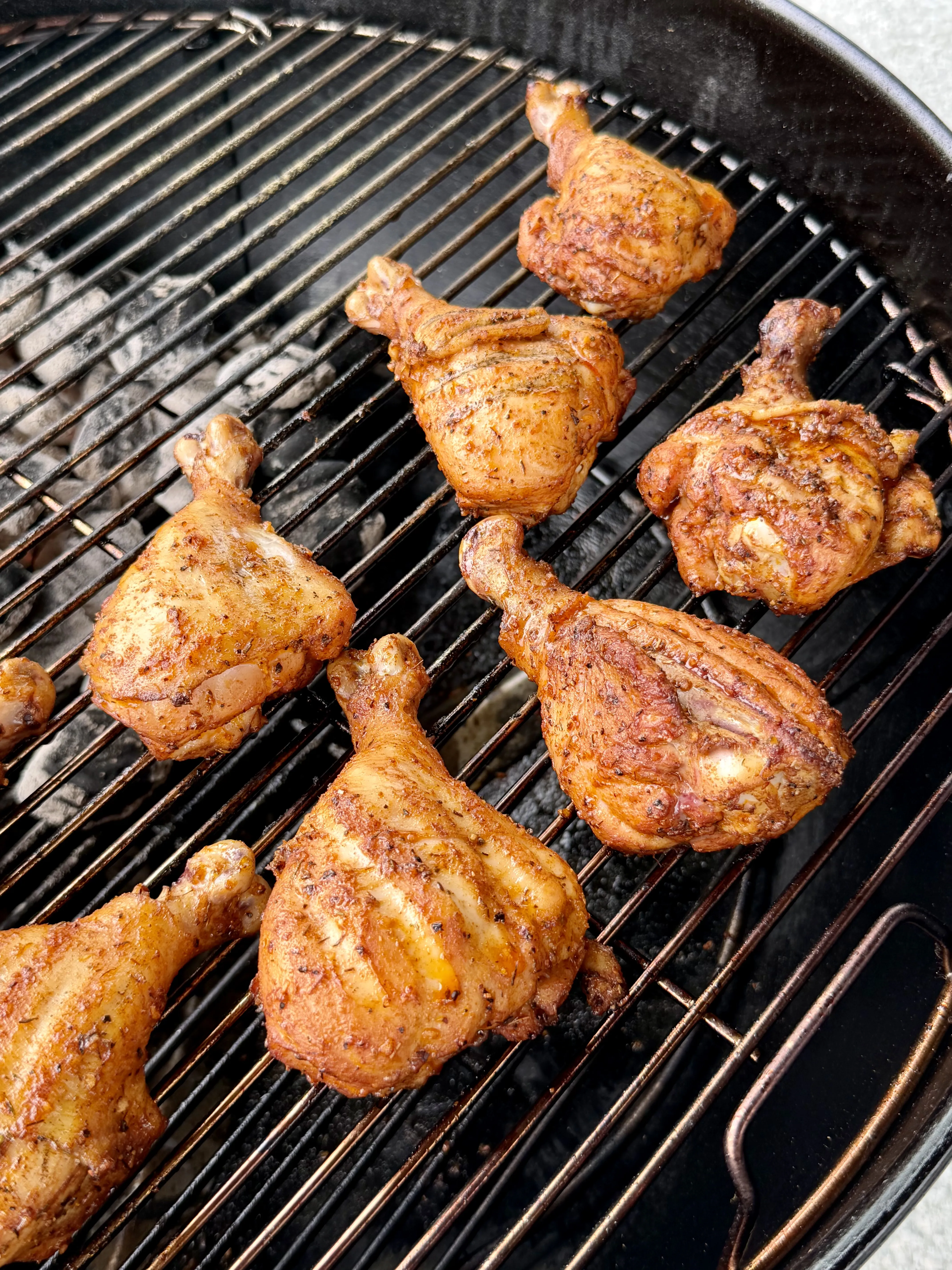 Seasoned Cajun chicken drumsticks grilling on a charcoal grill, golden-brown with spiced crust