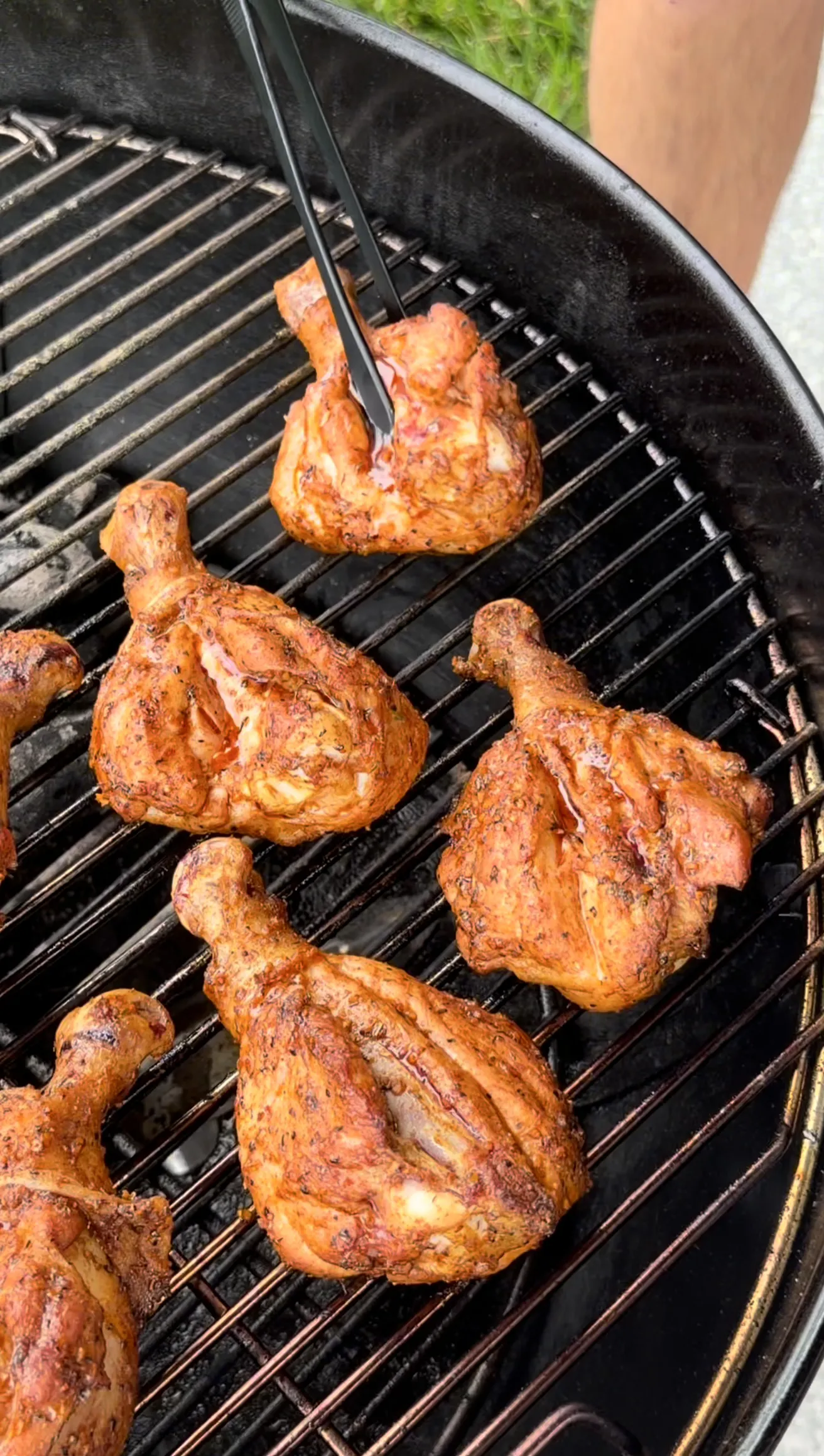 Seasoned Cajun chicken drumsticks grilling on a charcoal grill, being turned with tongs